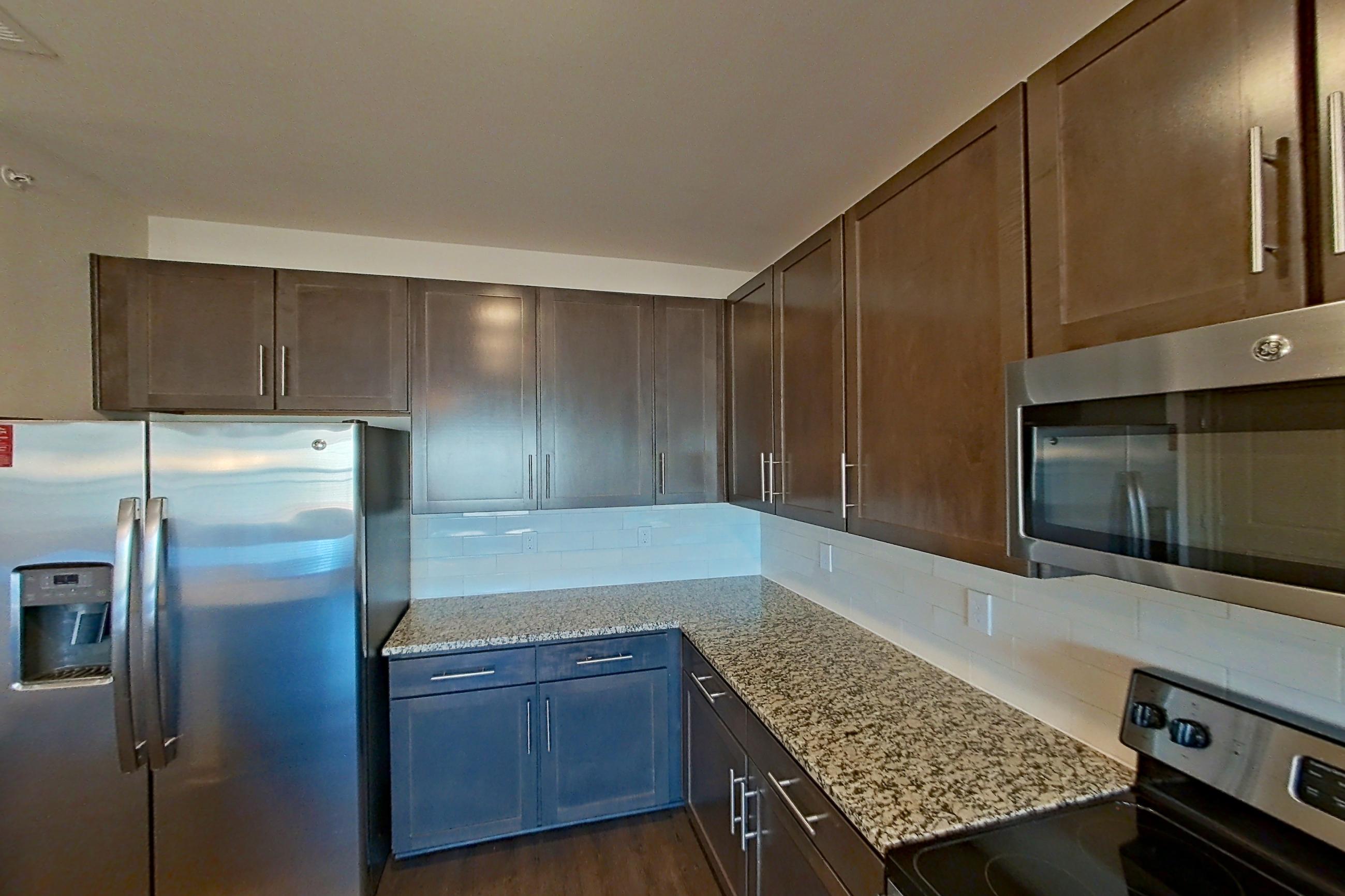 Kitchen with dark wood-finish flooring, dishwasher, electric range, light stone countertops, microwave, oven/range, refrigerator, stainless steel appliances, and water & ice dispenser, Apartment 1-506 at Aventine Northshore