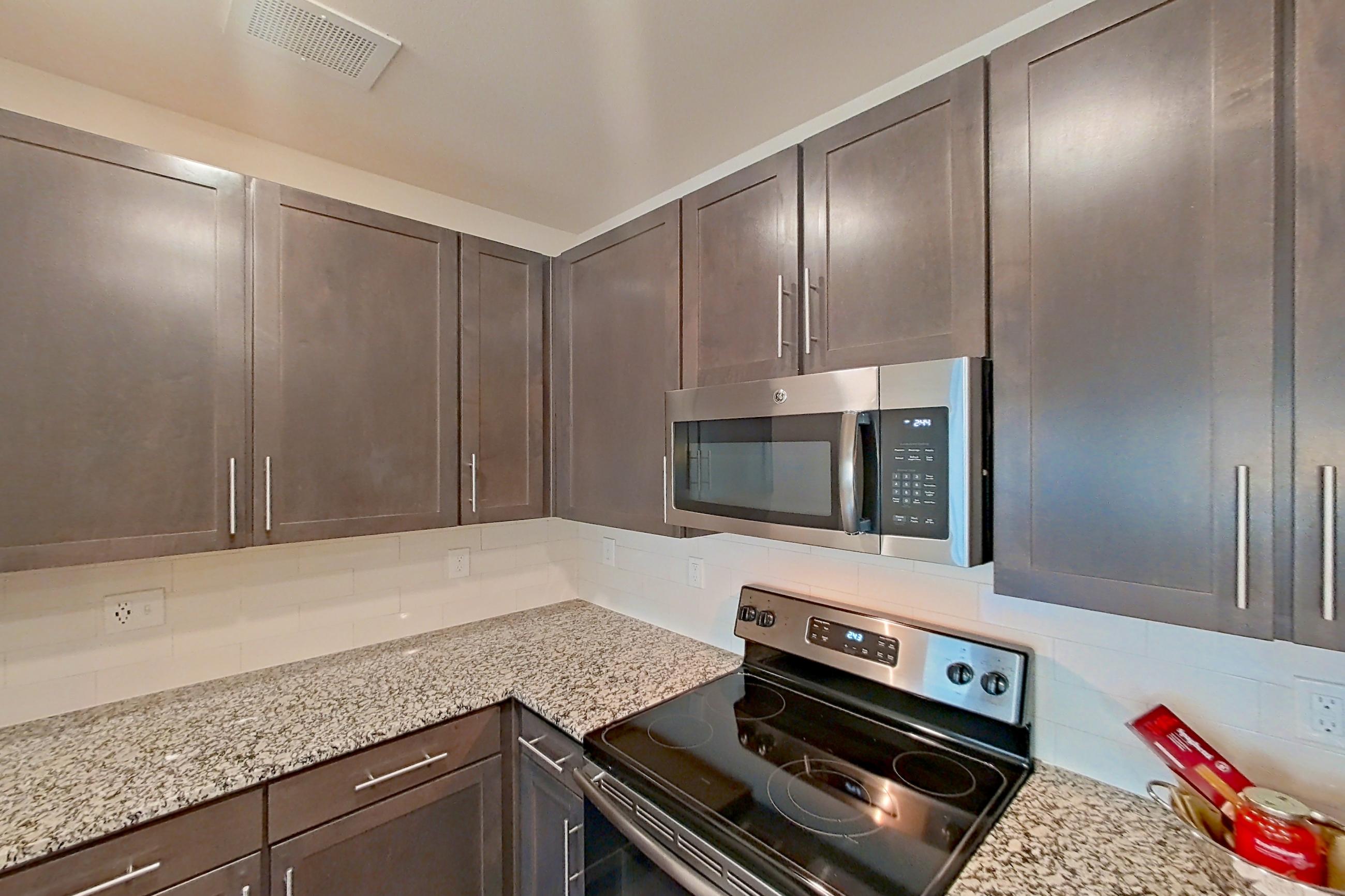 Kitchen with dark wood-finish flooring, dishwasher, electric range, light countertops, light stone countertops, microwave, oven/range, refrigerator, stainless steel appliances, and water & ice dispenser, Apartment 6-300 at Aventine Northshore