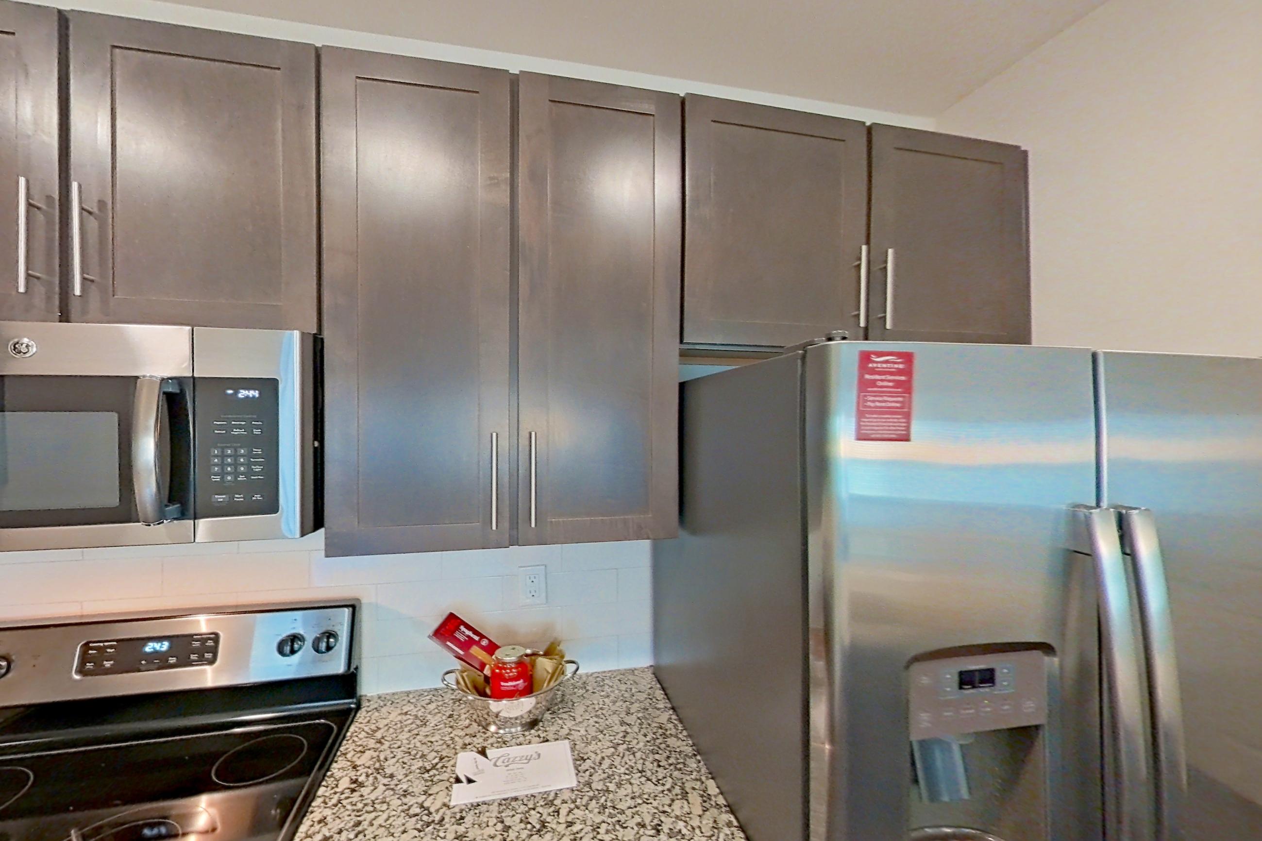 Kitchen with dark wood-finish flooring, dishwasher, electric range, light countertops, light stone countertops, microwave, oven/range, refrigerator, stainless steel appliances, and water & ice dispenser, Apartment 6-300 at Aventine Northshore