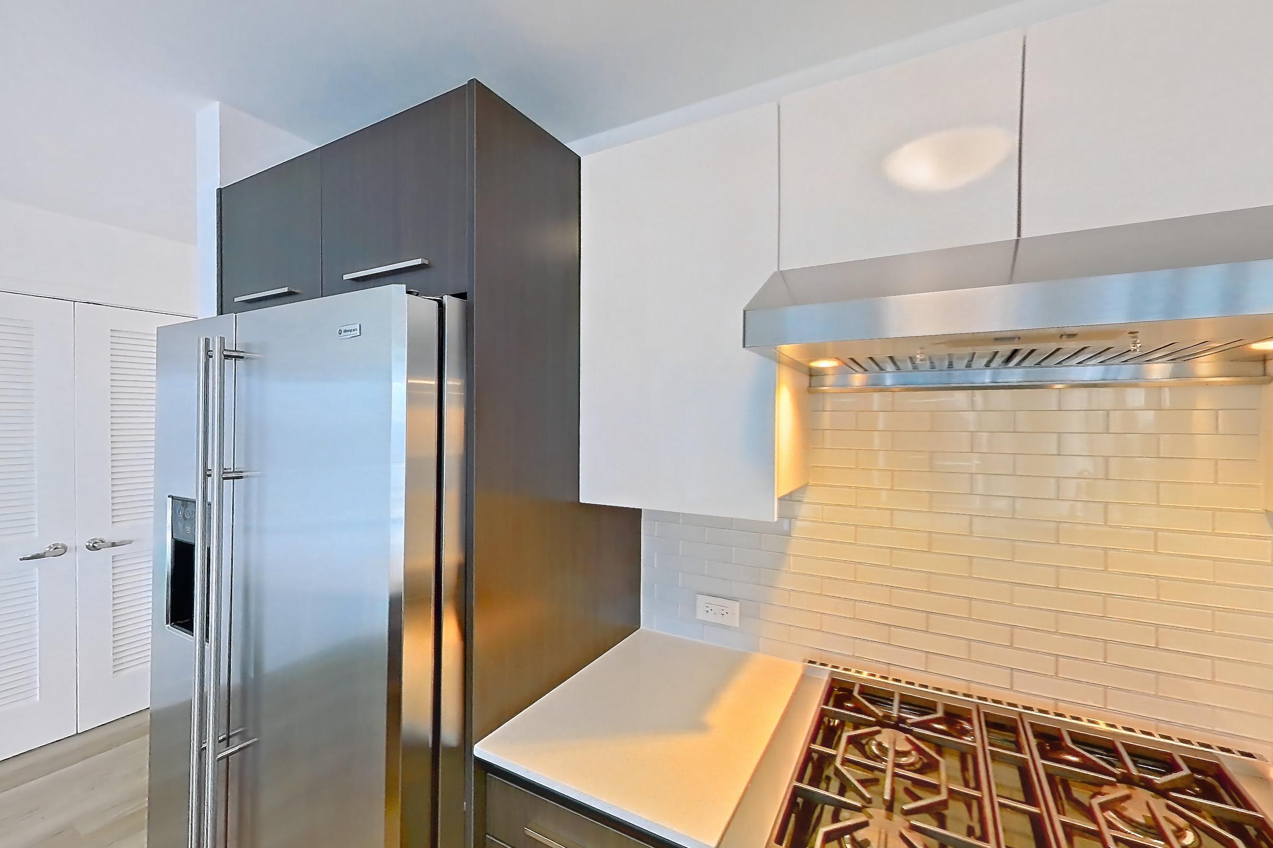 Kitchen with gas range, kitchen island, light countertops, light stone countertops, light wood-finish flooring, oven/range, range hood, and stainless steel appliances, Apartment 4307 at Wolf Point West