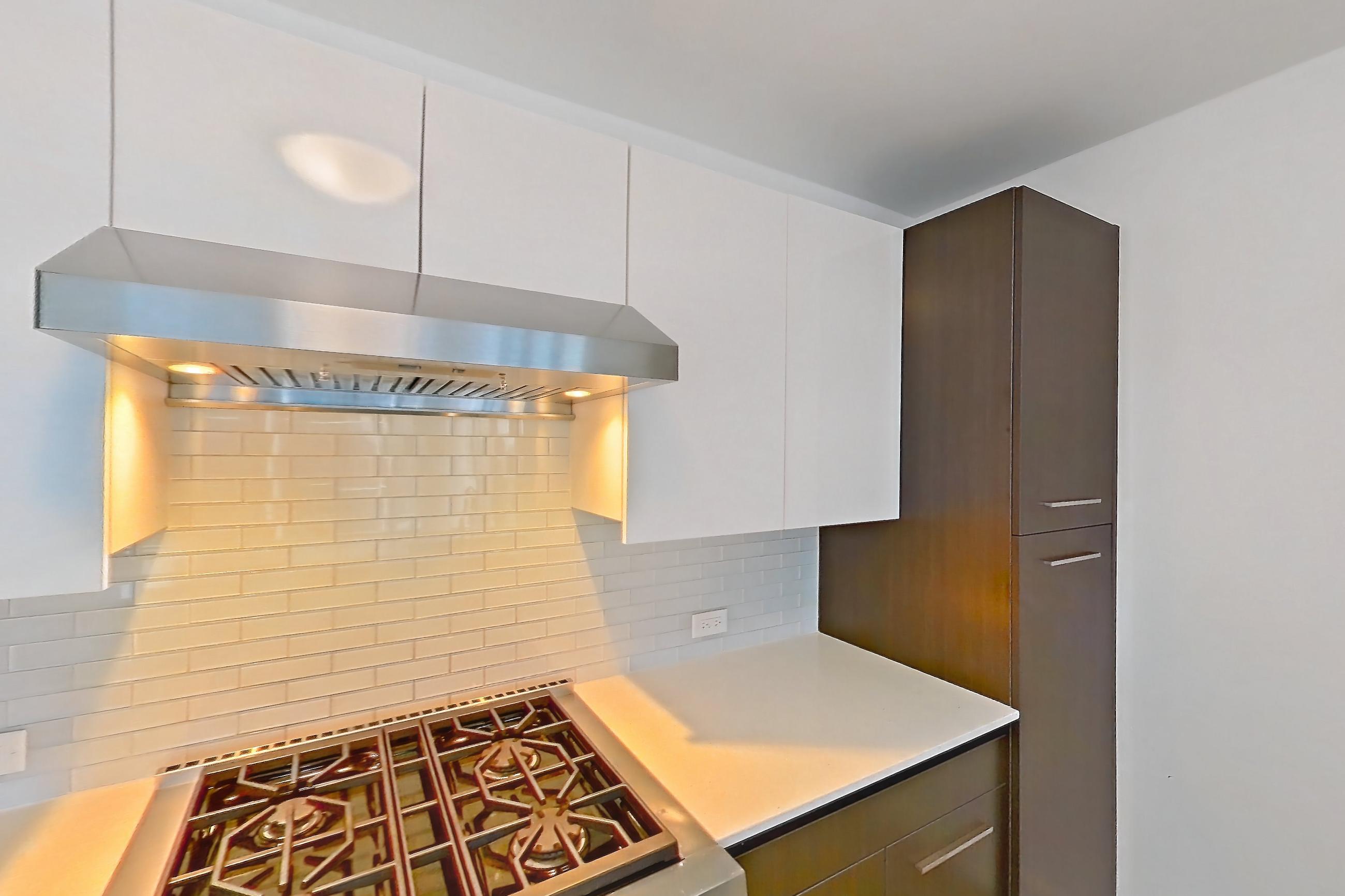 Kitchen with gas range, kitchen island, light countertops, light stone countertops, light wood-finish flooring, oven/range, range hood, and stainless steel appliances, Apartment 4307 at Wolf Point West
