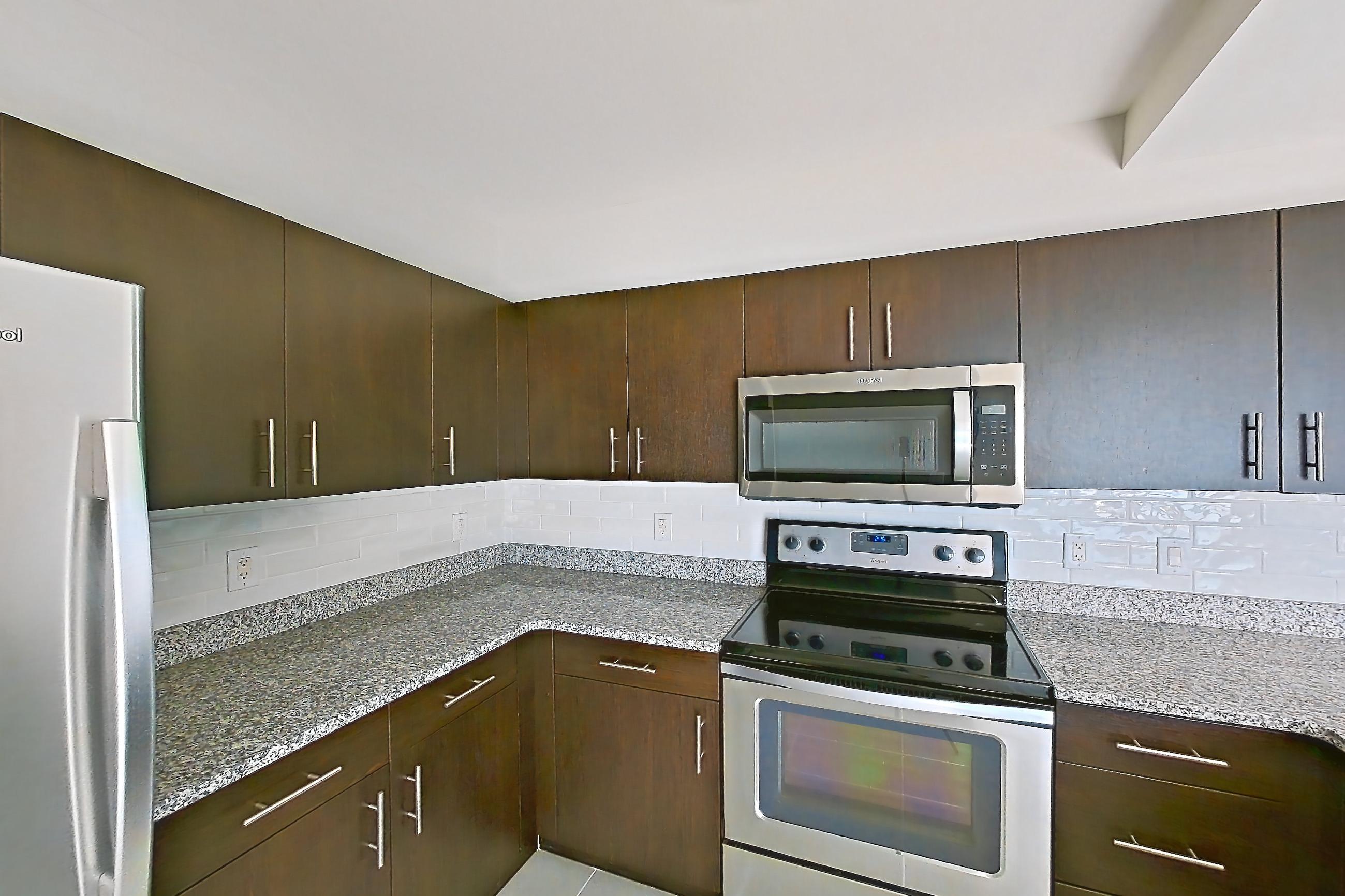 Kitchen with dark stone countertops, dishwasher, electric range, light stone countertops, light tile flooring, microwave, oven/range, refrigerator, and stainless steel appliances, Apartment RT-0922 at RiverTrace at Port Imperial