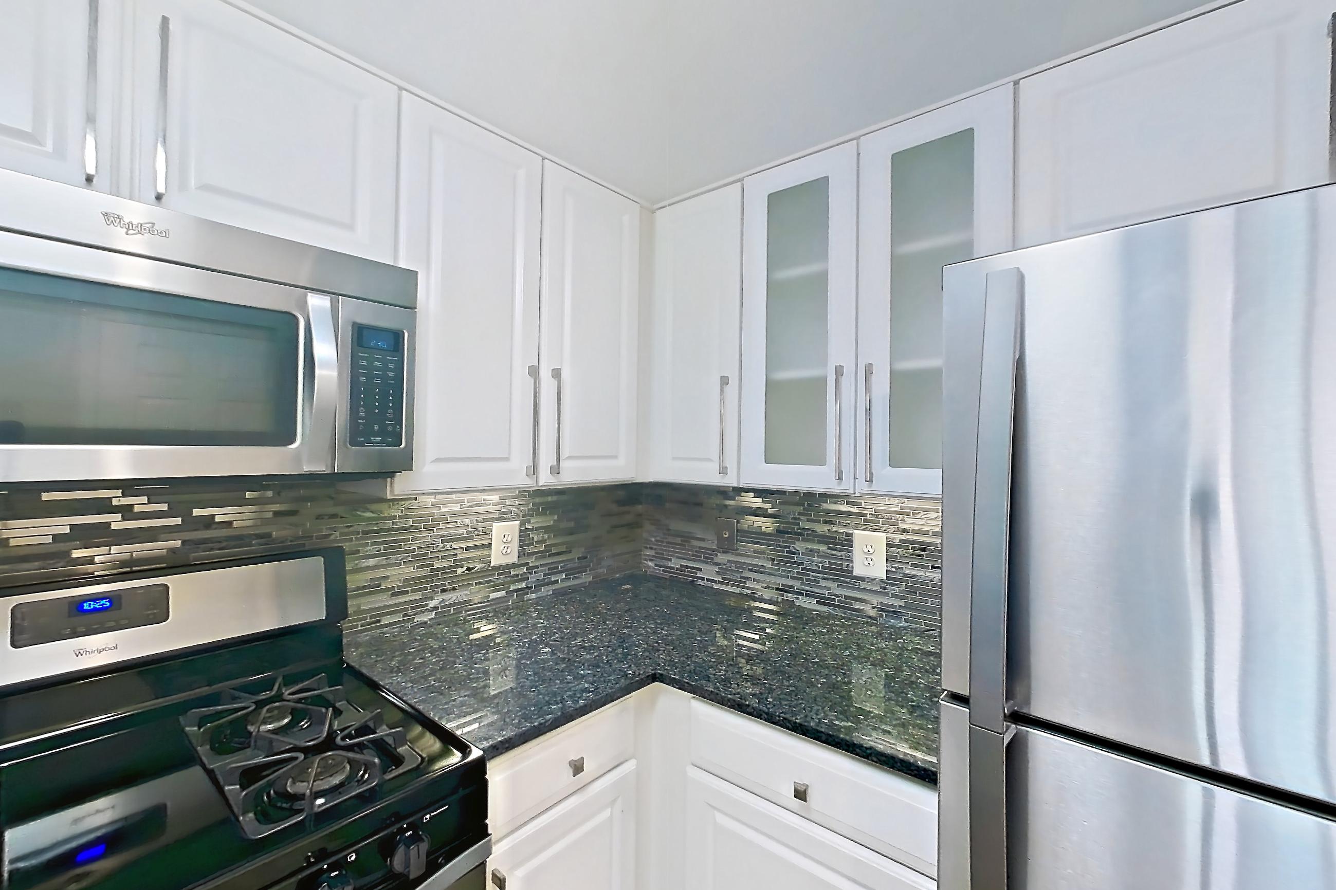 Kitchen with dark stone countertops, dishwasher, gas range, light countertops, light wood-finish flooring, oven/range, refrigerator, and stainless steel appliances, Apartment 1023 at The Barton at Woodley