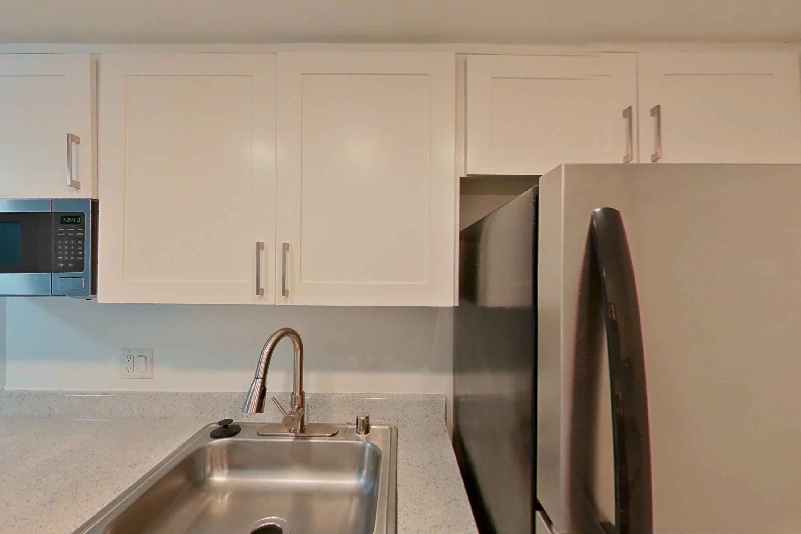 Kitchen with electric range, light countertops, light stone countertops, light wood-finish flooring, oven/range, range hood, refrigerator, and stainless steel appliances, Apartment 06 at Avana Rancho Cucamonga