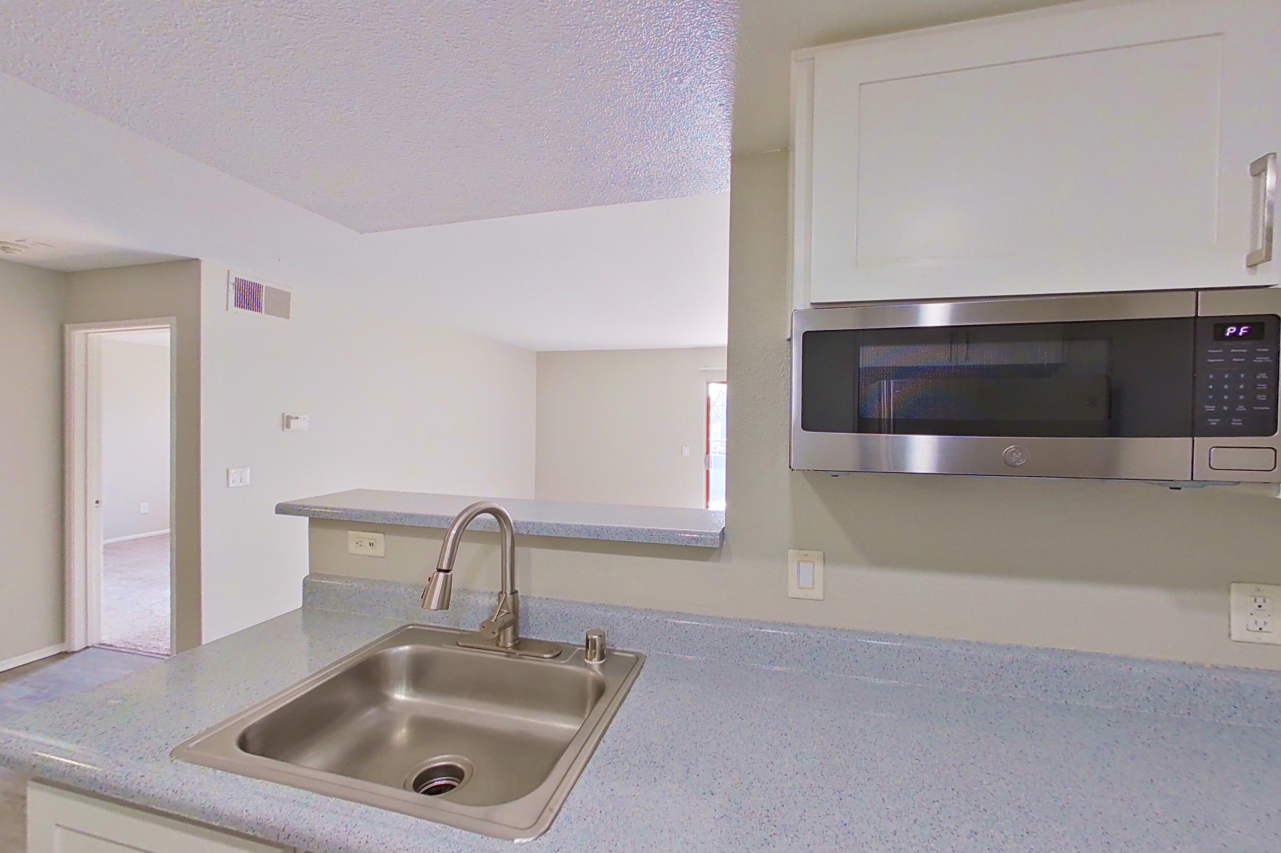 Kitchen with dishwasher, electric range, light countertops, light stone countertops, light wood-finish flooring, oven/range, range hood, refrigerator, and stainless steel appliances, Apartment 02 at Avana Rancho Cucamonga