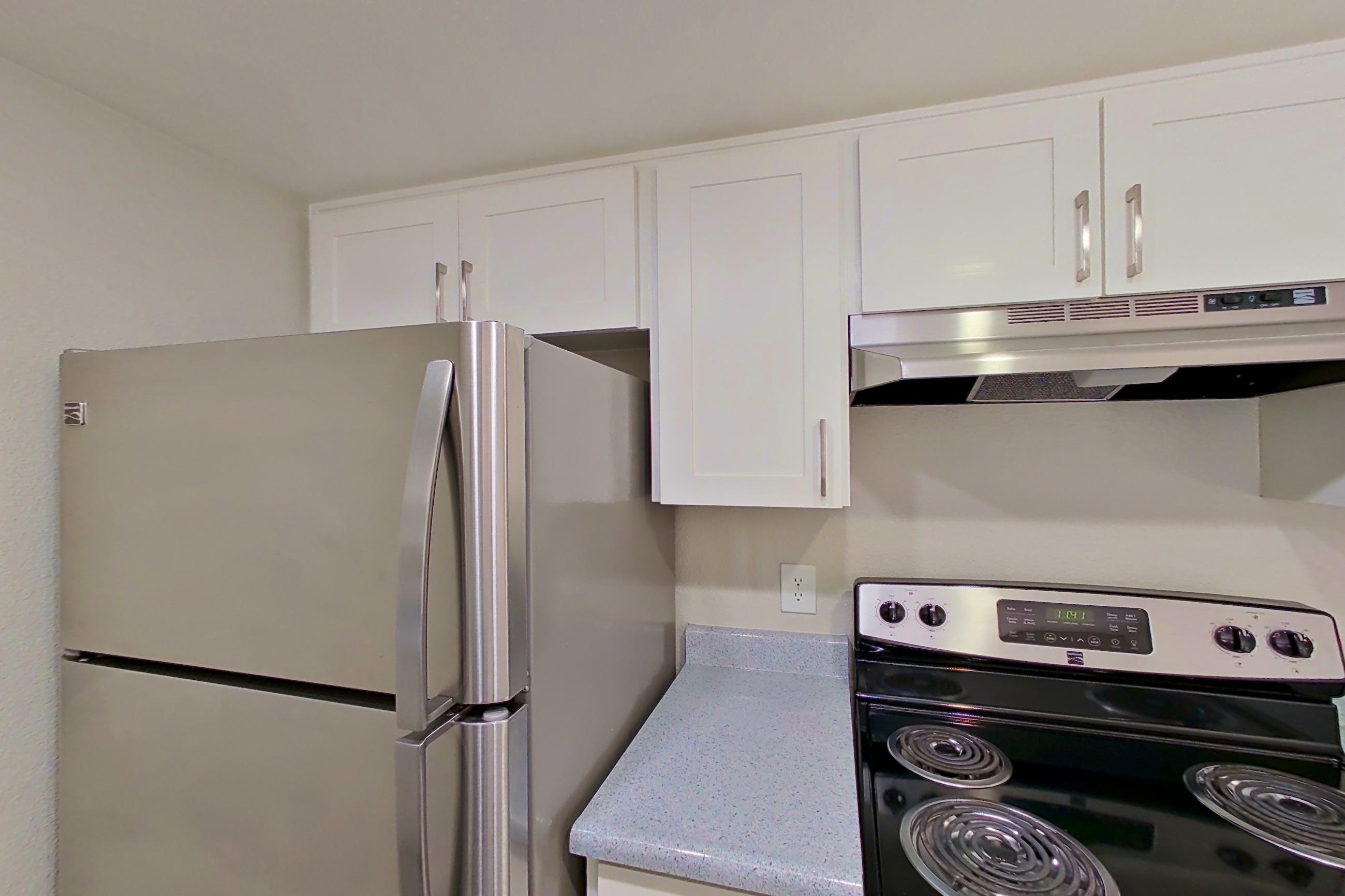 Kitchen with dishwasher, electric range, light countertops, light stone countertops, light wood-finish flooring, oven/range, range hood, refrigerator, and stainless steel appliances, Apartment 02 at Avana Rancho Cucamonga