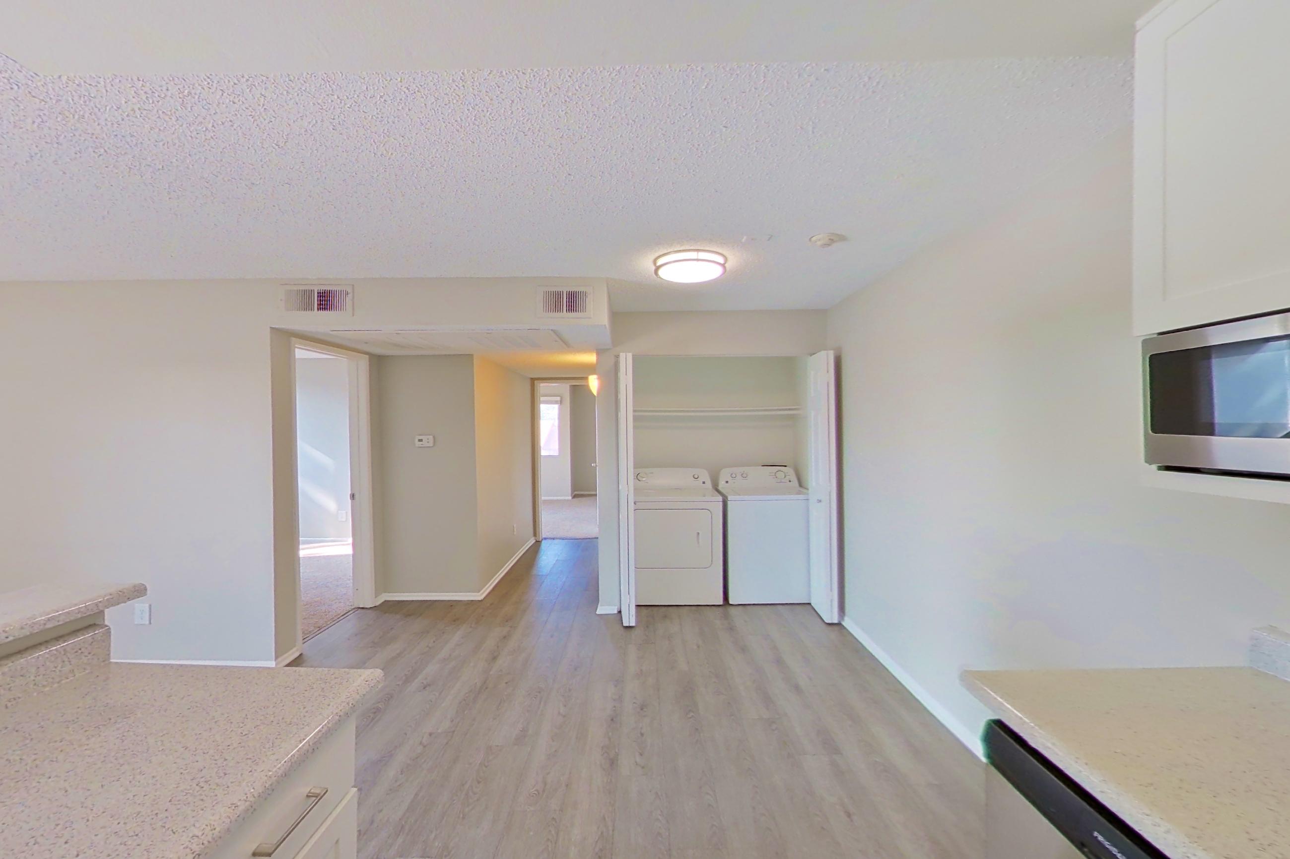 Kitchen with dishwasher, electric range, in-unit laundry, light countertops, light stone countertops, light wood-finish flooring, microwave, oven/range, range hood, and stainless steel appliances, Apartment 16-09 at Avana Rancho Cucamonga