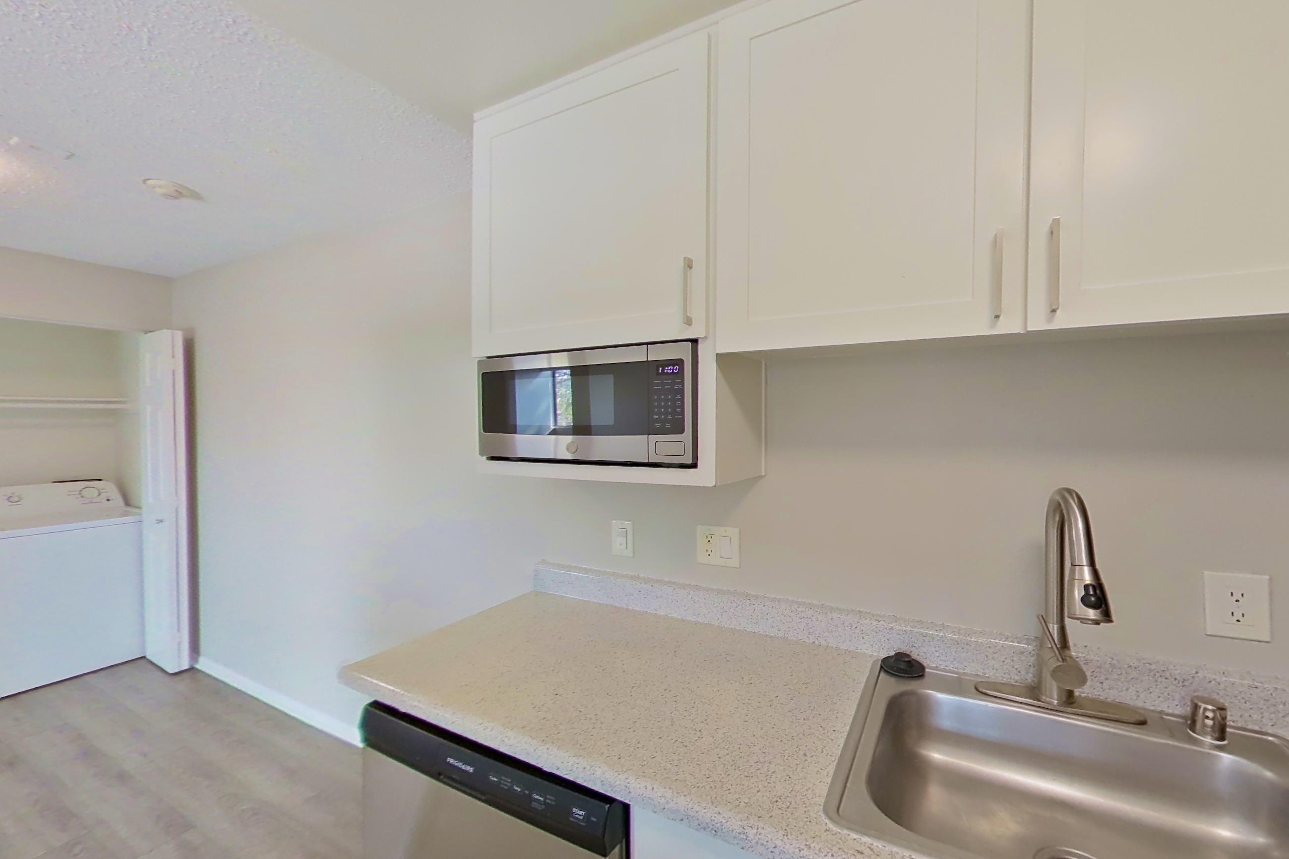 Kitchen with dishwasher, electric range, in-unit laundry, light countertops, light stone countertops, light wood-finish flooring, microwave, oven/range, range hood, and stainless steel appliances, Apartment 16-09 at Avana Rancho Cucamonga