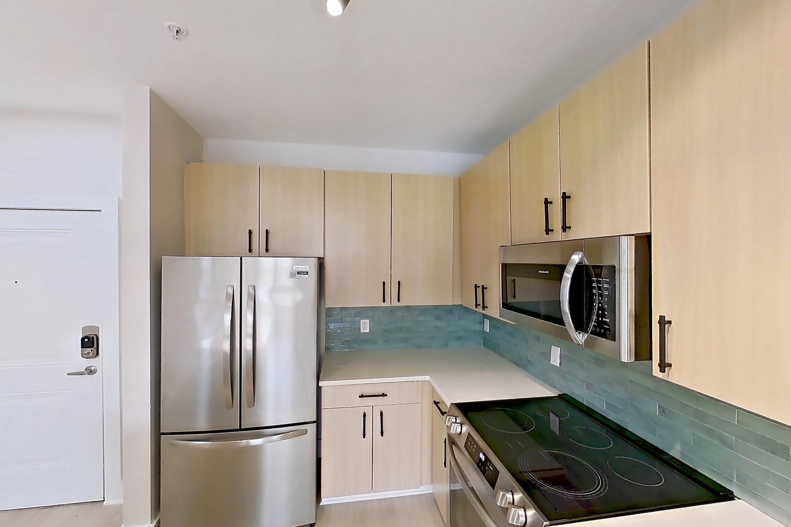 Kitchen with electric range, light countertops, light wood-finish flooring, microwave, oven/range, refrigerator, and stainless steel appliances, Apartment 3233 at NoHo Flats