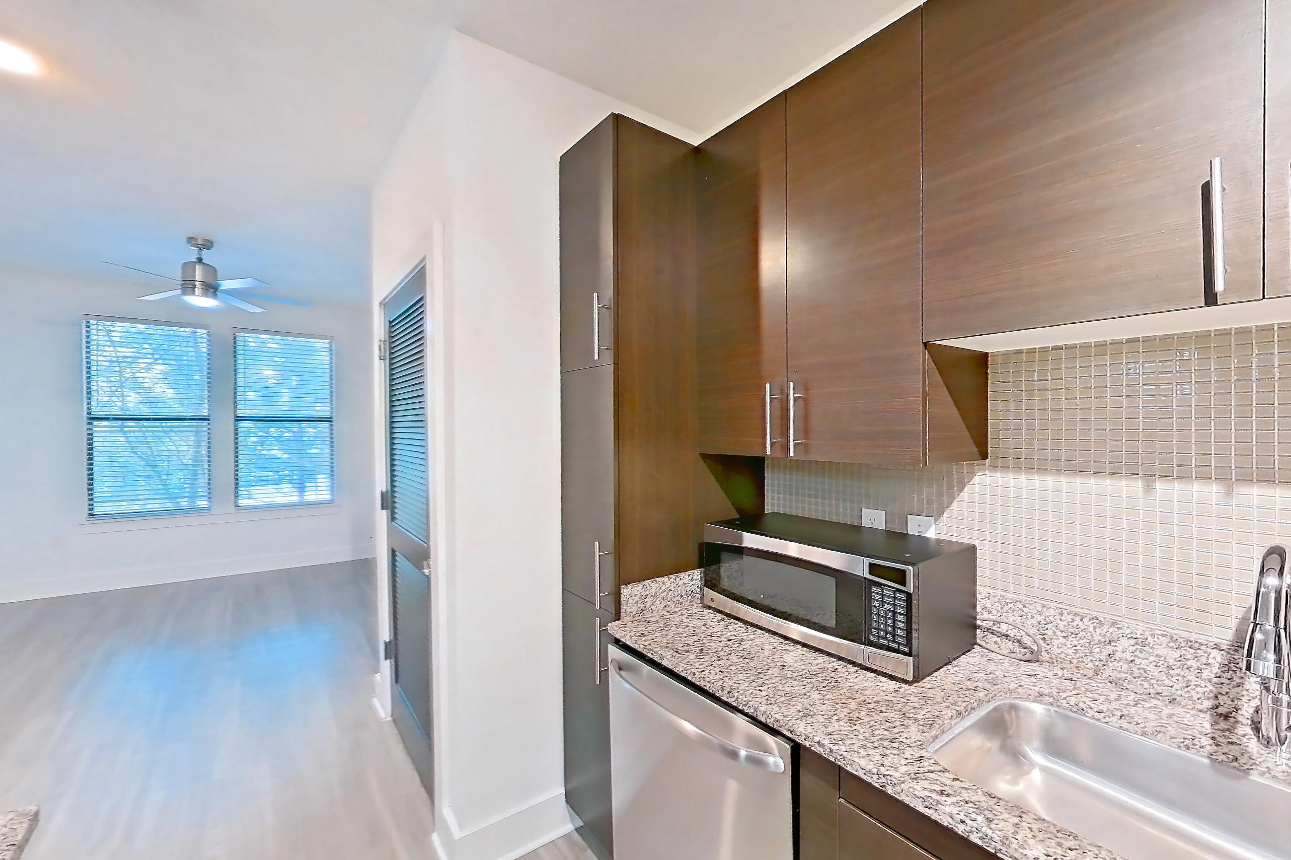 Kitchen with dishwasher, electric range, light stone countertops, light wood-finish flooring, microwave, oven/range, range hood, refrigerator, and stainless steel appliances, Apartment 4227 at NoHo Flats