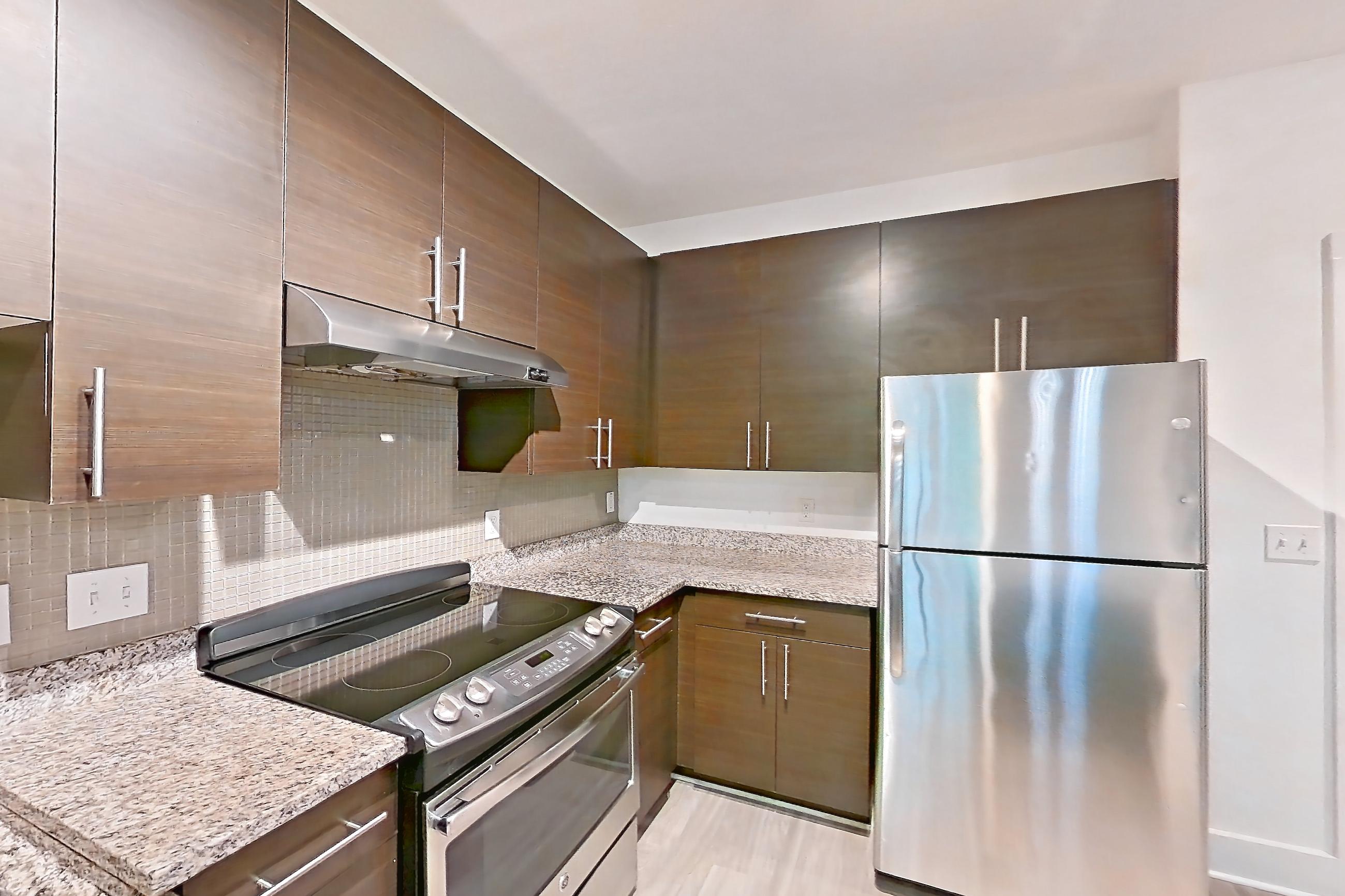 Kitchen with dishwasher, electric range, light stone countertops, light wood-finish flooring, microwave, oven/range, range hood, refrigerator, and stainless steel appliances, Apartment 4227 at NoHo Flats