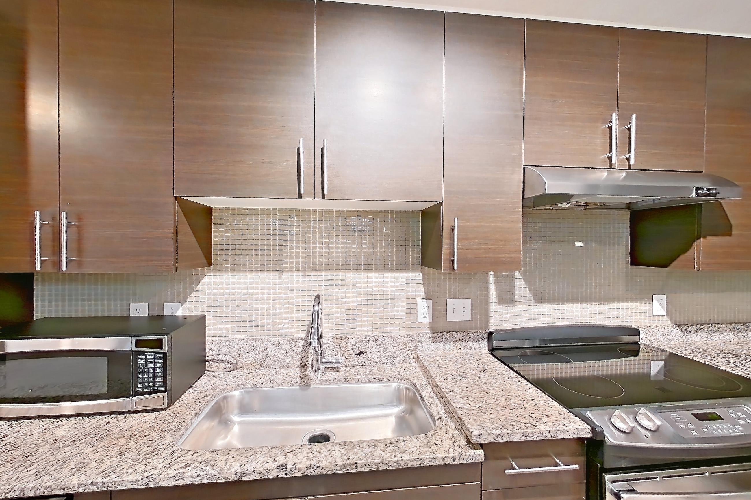 Kitchen with dishwasher, electric range, light stone countertops, light wood-finish flooring, microwave, oven/range, range hood, refrigerator, and stainless steel appliances, Apartment 4227 at NoHo Flats