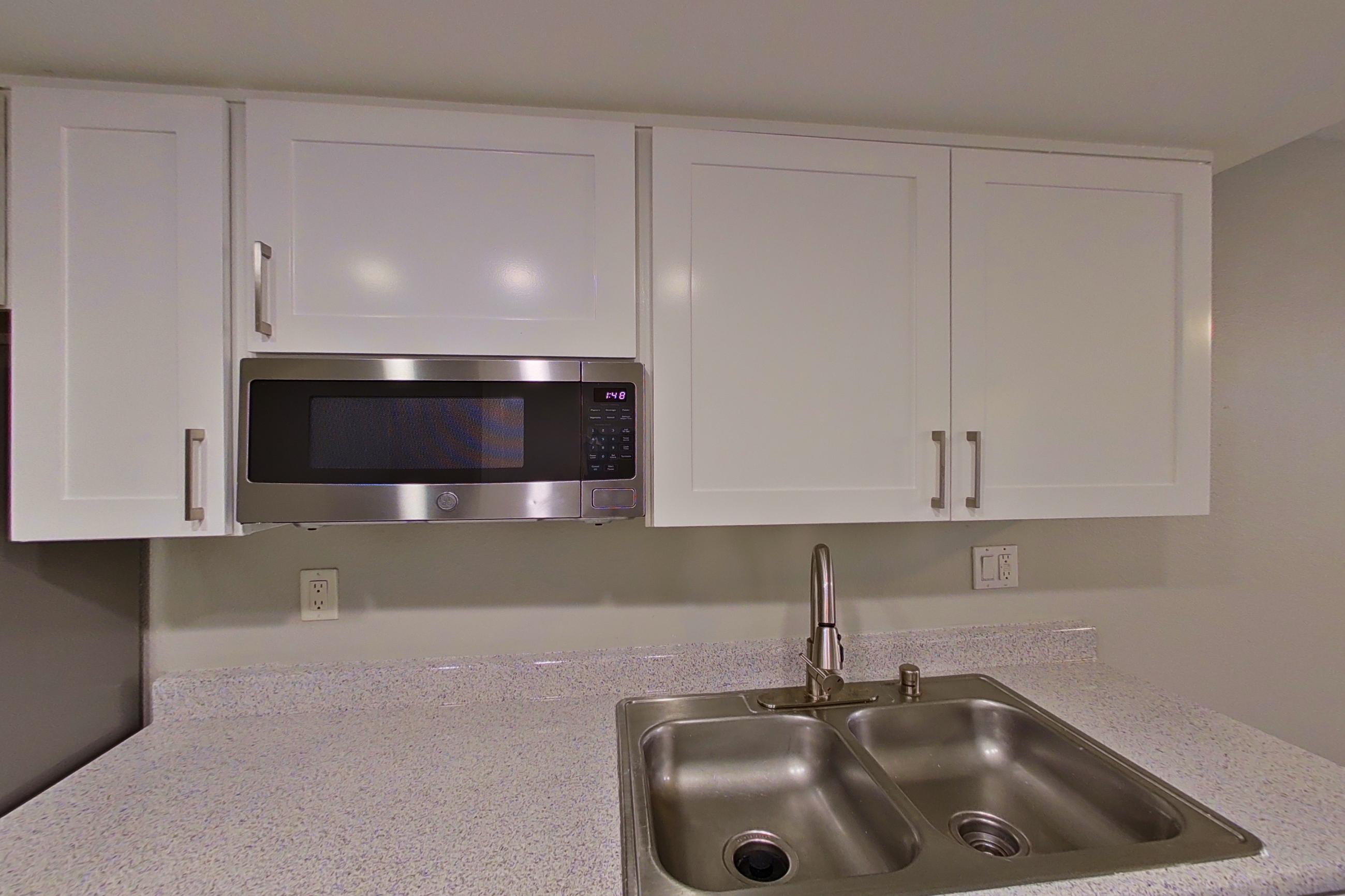 Kitchen with dishwasher, electric range, light countertops, light stone countertops, light wood-finish flooring, microwave, oven/range, refrigerator, and stainless steel appliances, Apartment 03 at Avana Rancho Cucamonga
