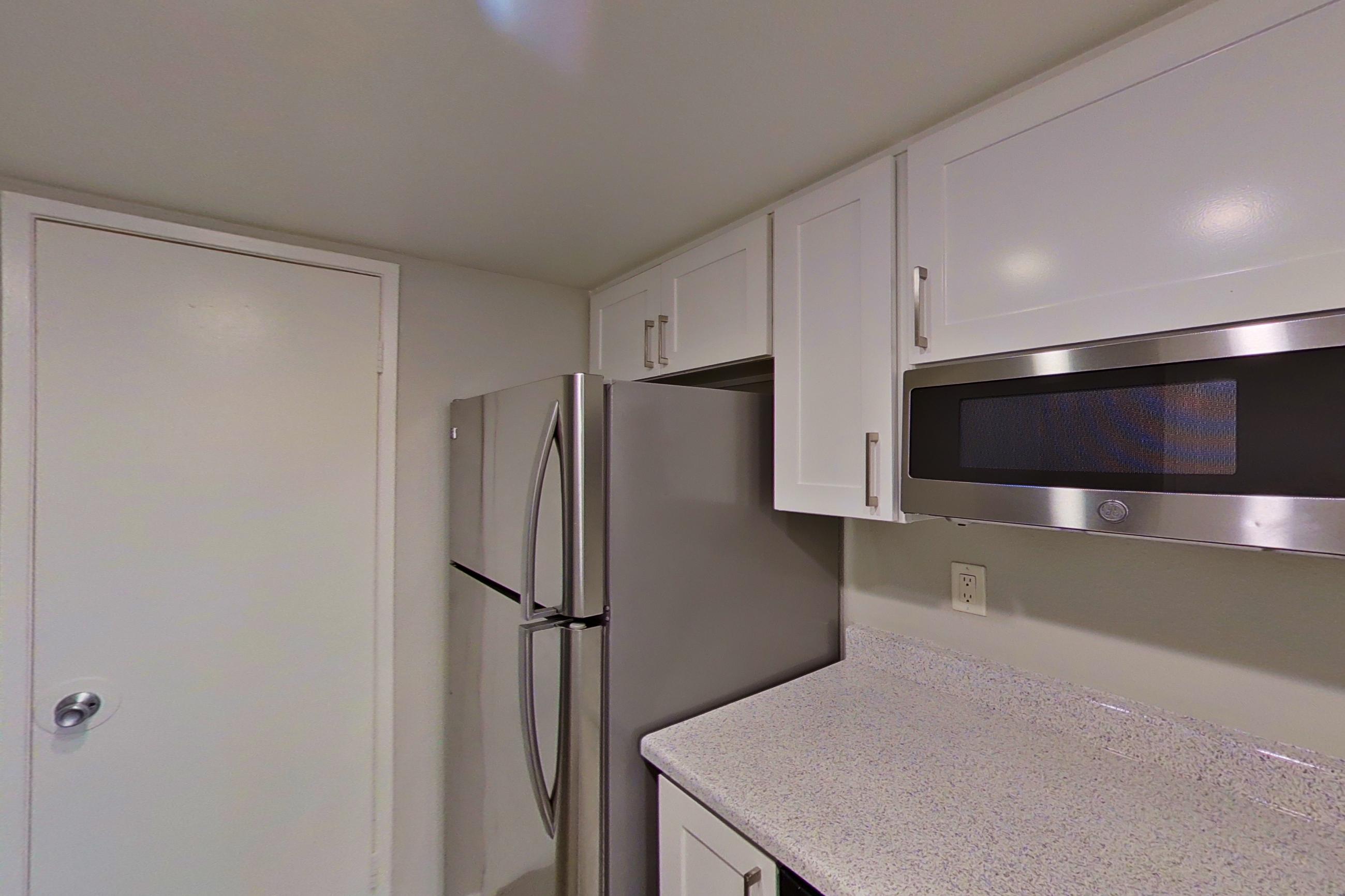 Kitchen with dishwasher, electric range, light countertops, light stone countertops, light wood-finish flooring, microwave, oven/range, refrigerator, and stainless steel appliances, Apartment 03 at Avana Rancho Cucamonga