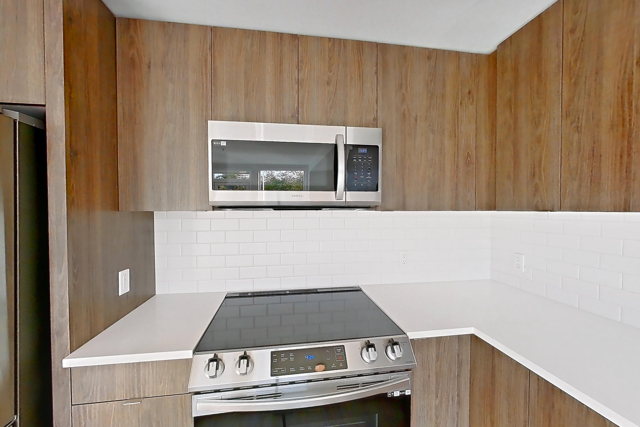 Kitchen with dishwasher, electric range, light countertops, light stone countertops, light wood-finish flooring, microwave, mini-split AC, oven/range, and stainless steel appliances, Apartment 416 at The Cline