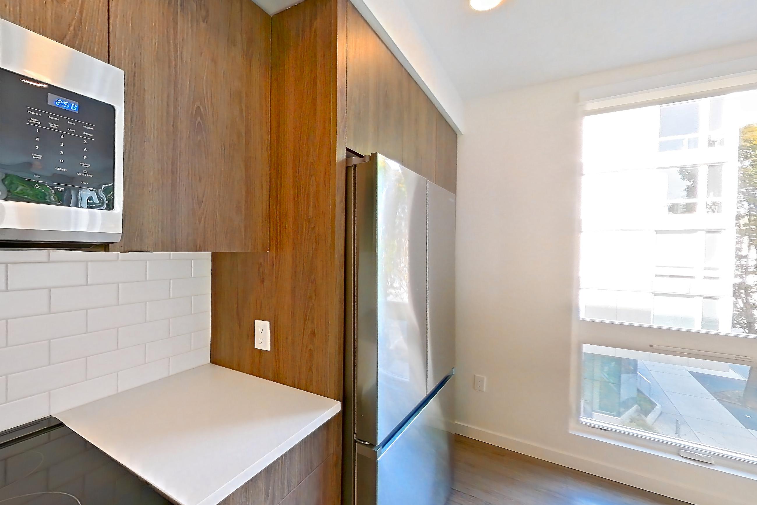 Kitchen with cooktop, dishwasher, electric cooktop, electric range, light countertops, light stone countertops, light wood-finish flooring, microwave, oven/range, refrigerator, and stainless steel appliances, Apartment 403 at The Cline