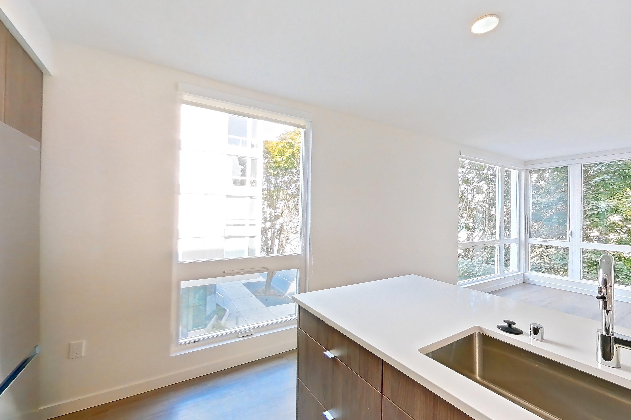 Kitchen with cooktop, dishwasher, electric cooktop, electric range, light countertops, light stone countertops, light wood-finish flooring, microwave, oven/range, refrigerator, and stainless steel appliances, Apartment 403 at The Cline