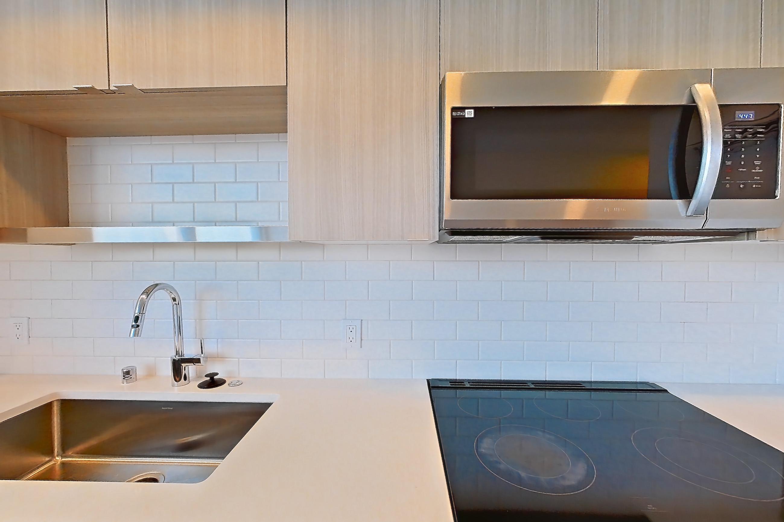 Kitchen with dishwasher, electric range, light countertops, light stone countertops, light wood-finish flooring, microwave, mini-split AC, oven/range, refrigerator, and stainless steel appliances, Apartment 733 at The Cline