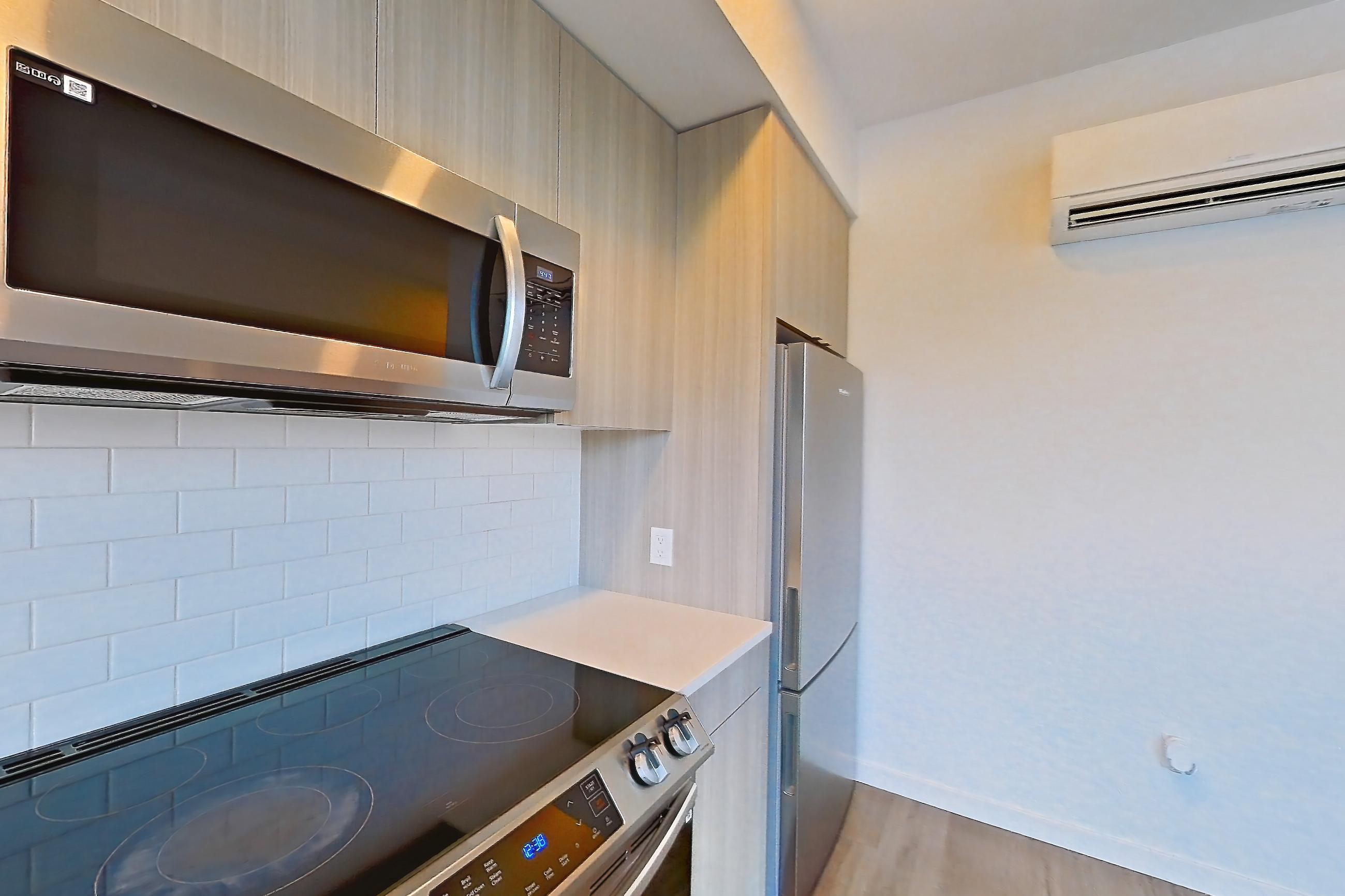 Kitchen with dishwasher, electric range, light countertops, light stone countertops, light wood-finish flooring, microwave, mini-split AC, oven/range, refrigerator, and stainless steel appliances, Apartment 733 at The Cline