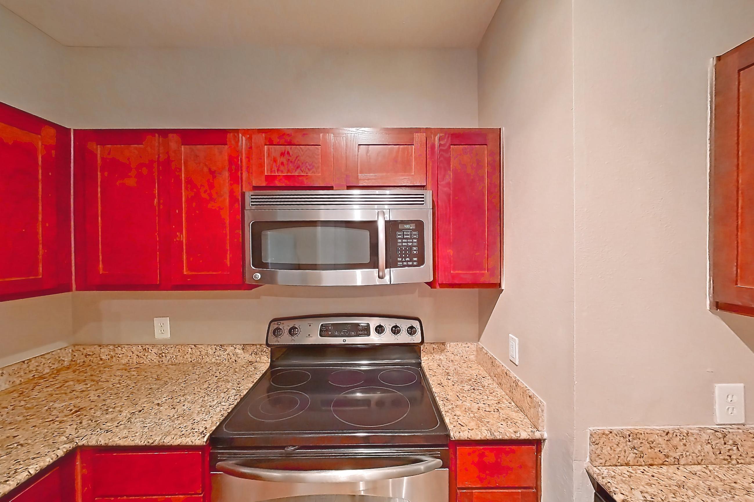 Kitchen with dishwasher, electric range, light stone countertops, light wood-finish flooring, microwave, oven/range, refrigerator, and stainless steel appliances, Apartment 0214 at Marquis at Barton Trails I
