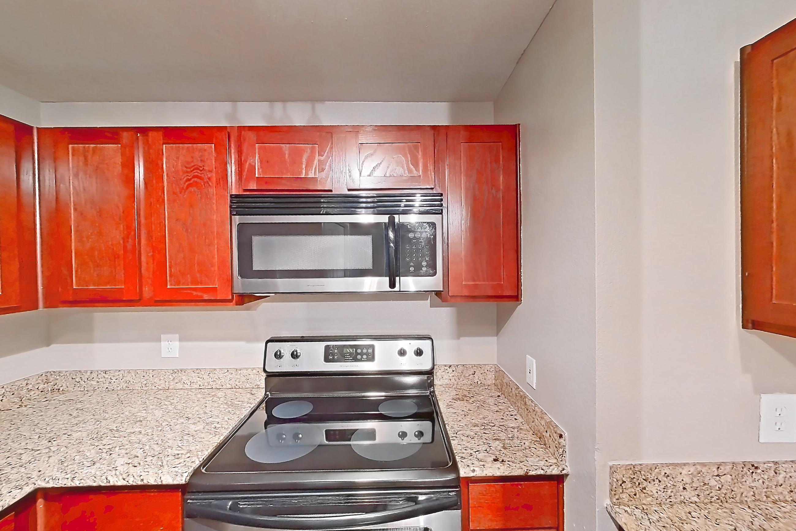 Kitchen with black appliances, dark wood-finish flooring, dishwasher, electric range, light stone countertops, microwave, oven/range, refrigerator, and stainless steel appliances, Apartment 0309 at Marquis at Barton Trails I