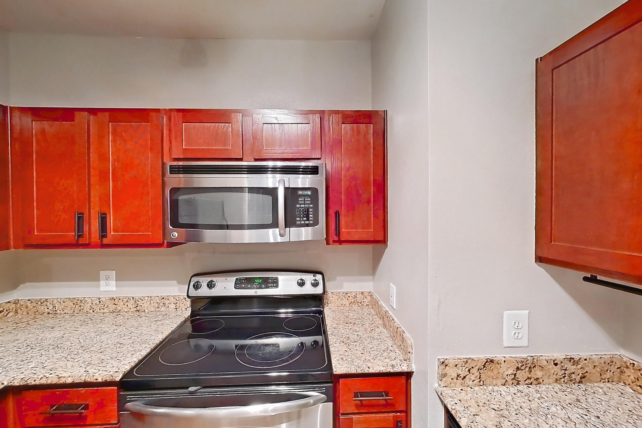 Kitchen with dishwasher, electric range, light stone countertops, light wood-finish flooring, microwave, oven/range, refrigerator, and stainless steel appliances, Apartment 0613 at Marquis at Barton Trails I