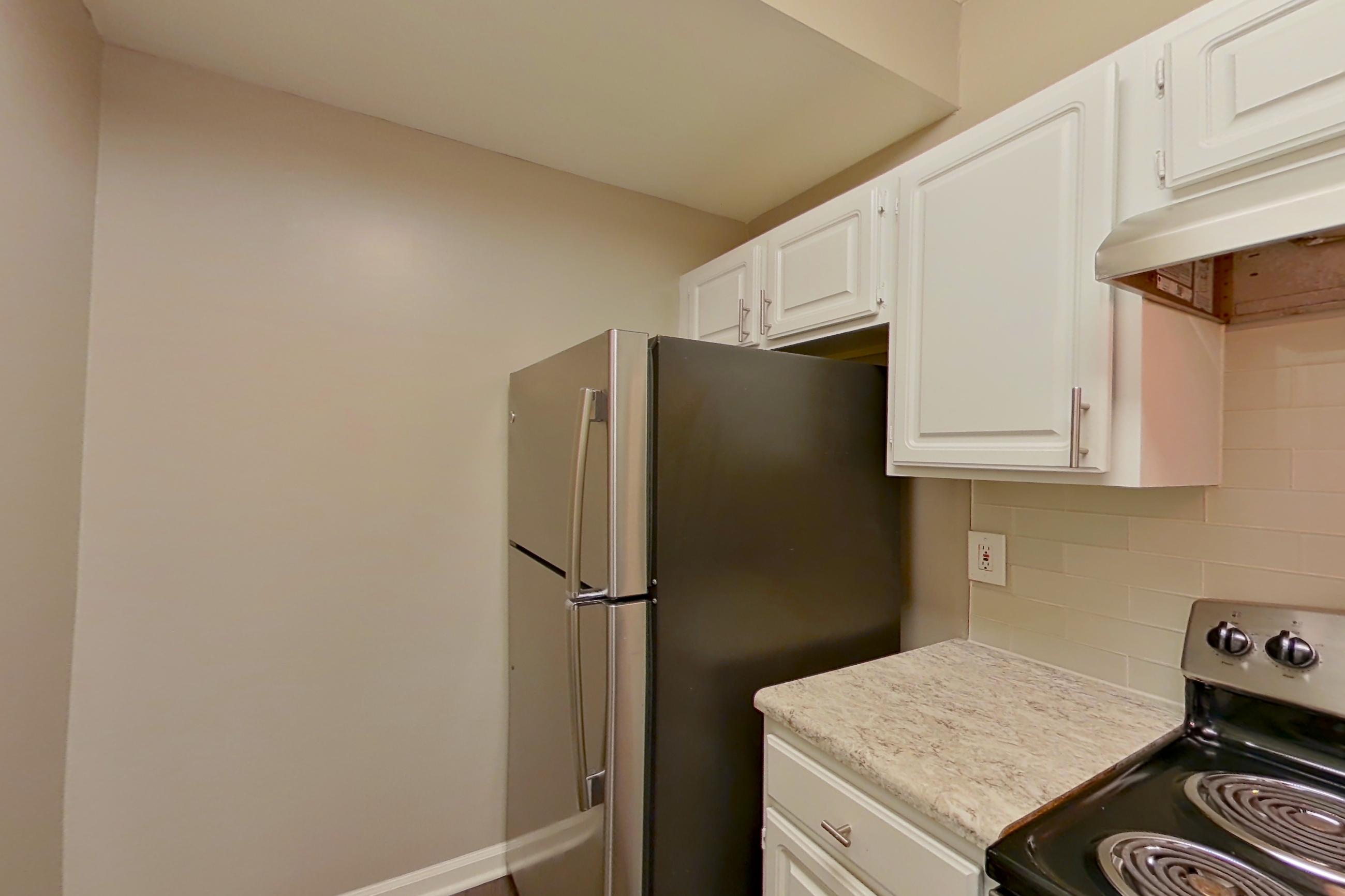 Kitchen with dark wood-finish flooring, dishwasher, electric range, light countertops, light stone countertops, oven/range, refrigerator, and stainless steel appliances, Apartment 0120 at The Marq at Brookhaven