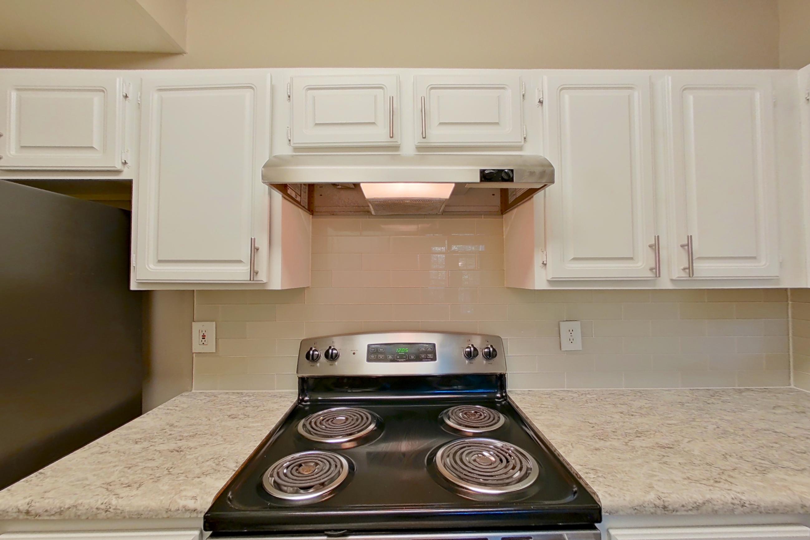 Kitchen with dark wood-finish flooring, dishwasher, electric range, light countertops, light stone countertops, oven/range, refrigerator, and stainless steel appliances, Apartment 0120 at The Marq at Brookhaven