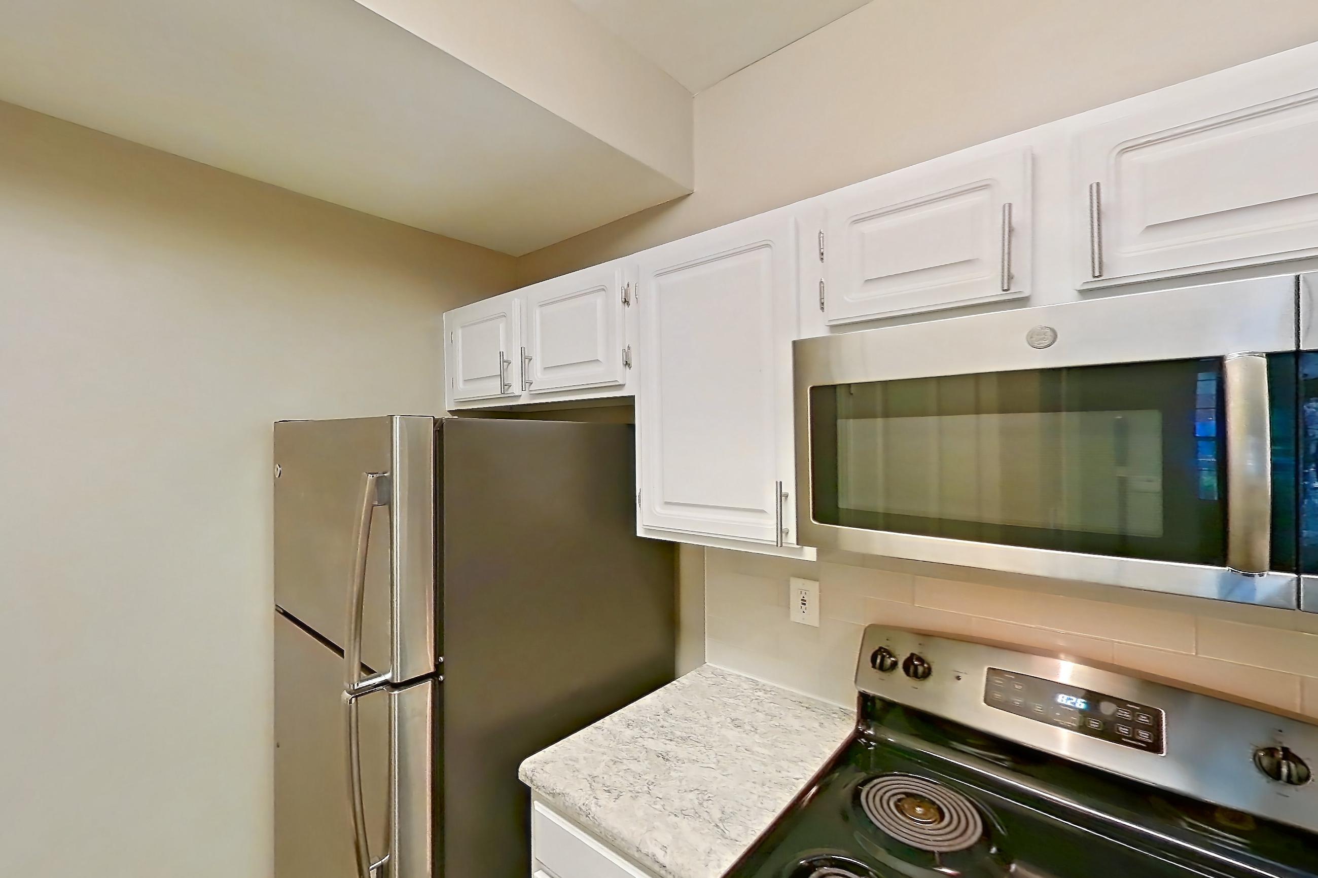 Kitchen with dark wood-finish flooring, dishwasher, electric range, light countertops, light stone countertops, microwave, oven/range, refrigerator, and stainless steel appliances, Apartment 0209 at The Marq at Brookhaven