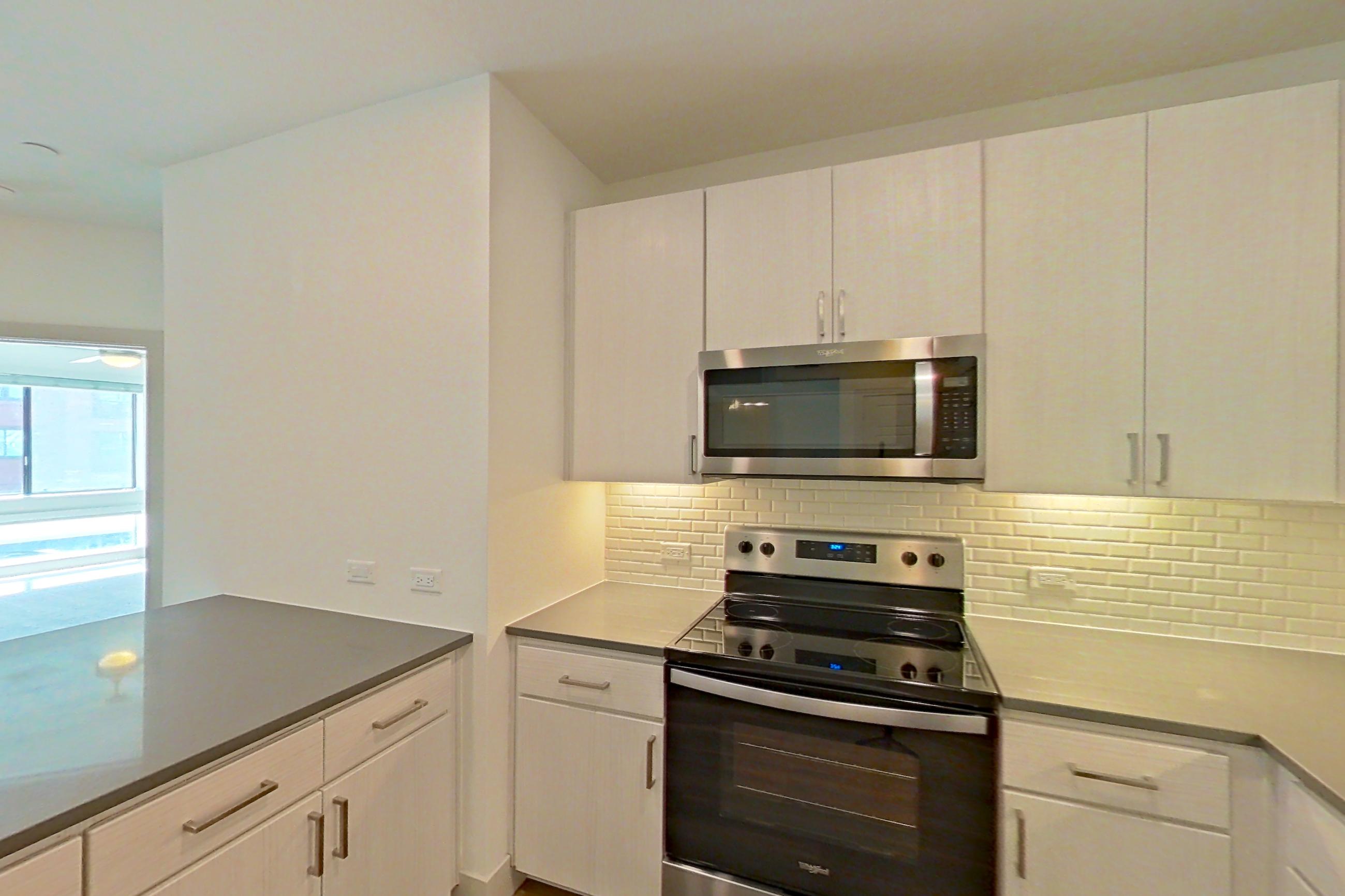 Kitchen with dark countertops, dark wood-finish flooring, dishwasher, electric range, light countertops, microwave, oven/range, and stainless steel appliances, Apartment 2090 at Marquis at Chandler