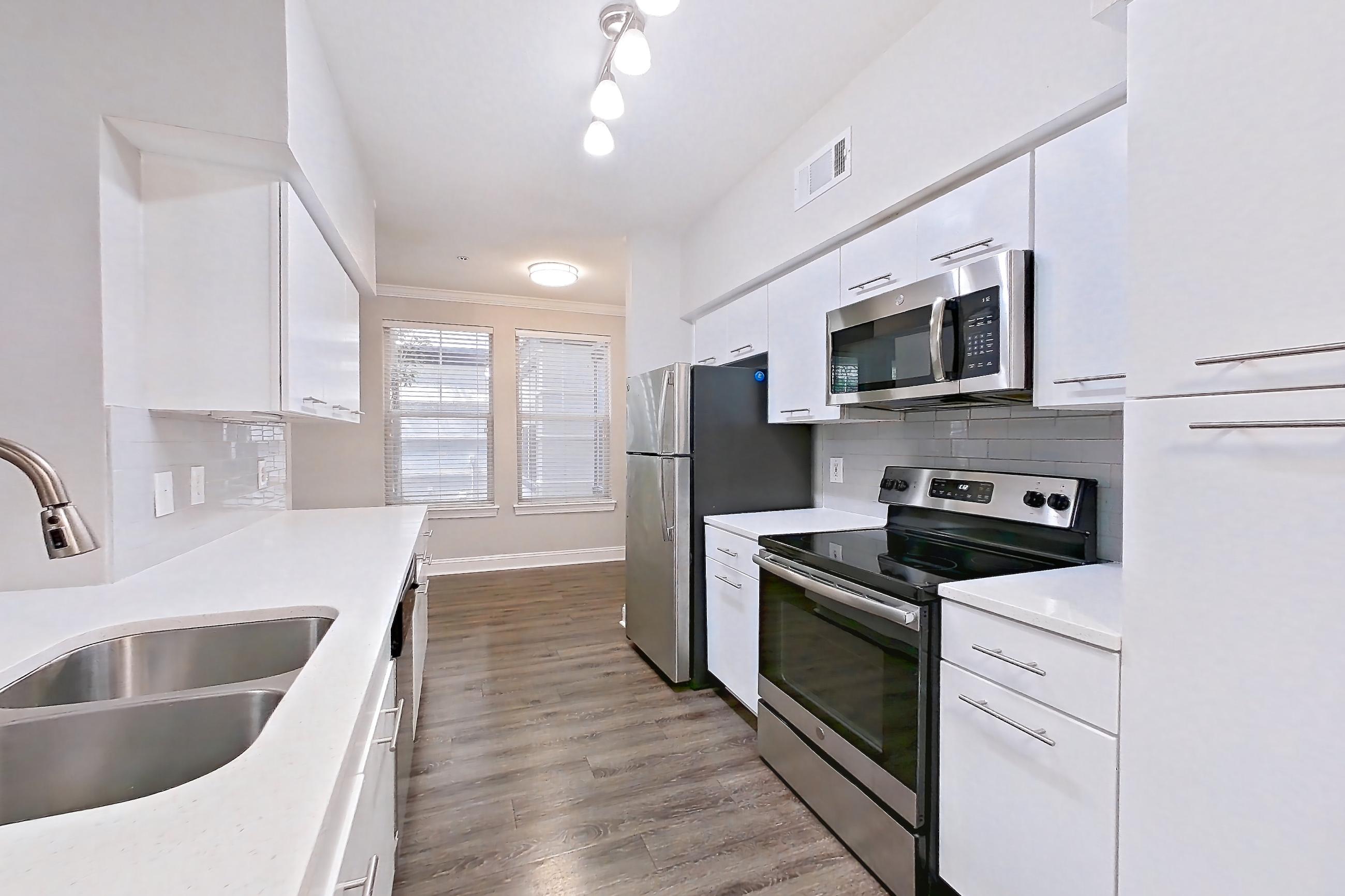 Kitchen with dark wood-finish flooring, electric range, in-unit laundry, light countertops, light stone countertops, light wood-finish flooring, microwave, oven/range, refrigerator, and stainless steel appliances, Apartment 1102 at Marq Perimeter