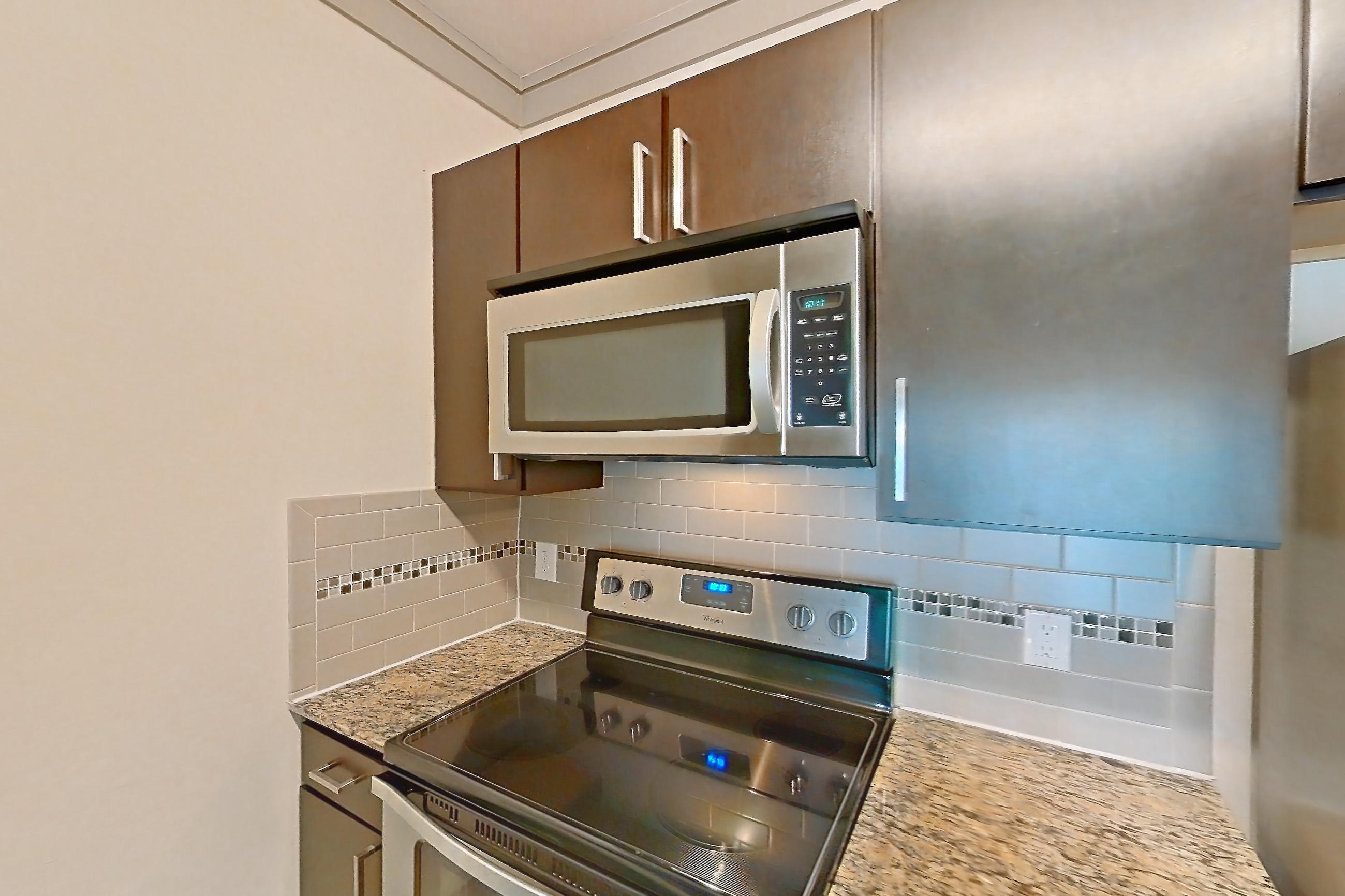 Kitchen with dishwasher, electric range, light stone countertops, light wood-finish flooring, microwave, oven/range, refrigerator, and stainless steel appliances, Apartment 1314 at Marquis Seven Meadows