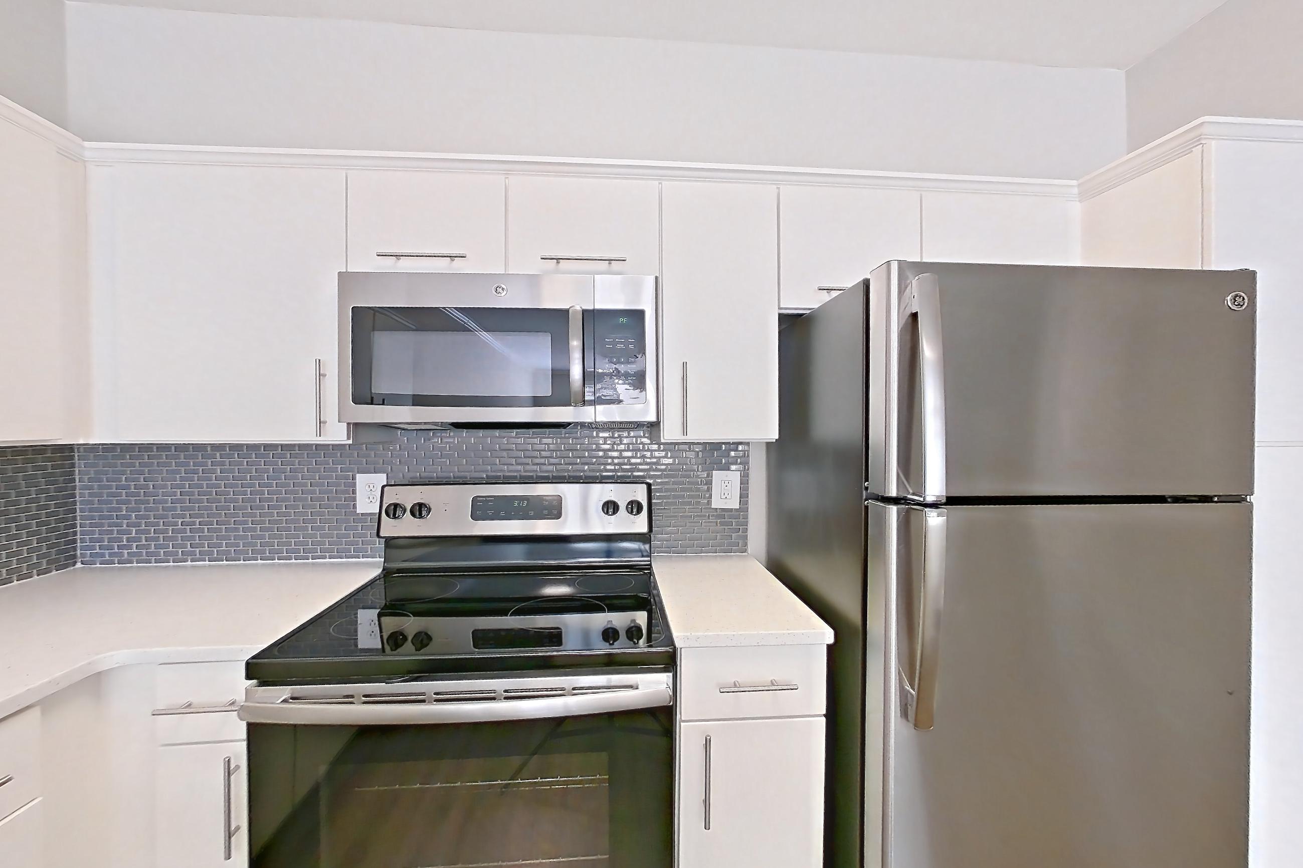 Kitchen with dishwasher, electric range, light countertops, light wood-finish flooring, microwave, oven/range, refrigerator, and stainless steel appliances, Apartment 2114 at Marq Perimeter