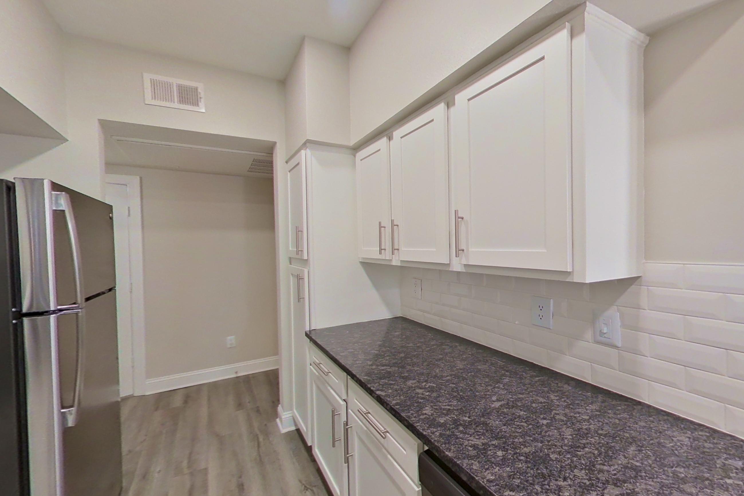 Kitchen with dark stone countertops, dishwasher, electric range, light countertops, light wood-finish flooring, microwave, oven/range, refrigerator, and stainless steel appliances, Apartment 2211 at Marq Perimeter