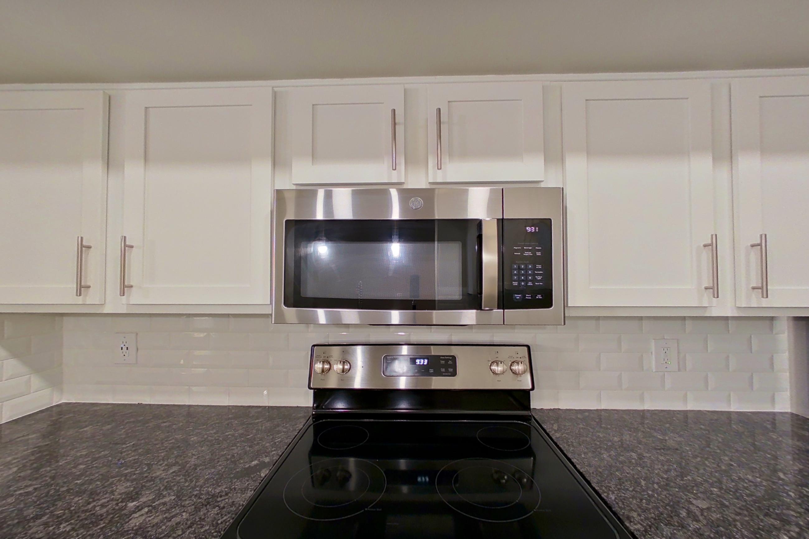 Kitchen with dark stone countertops, dishwasher, electric range, light countertops, light wood-finish flooring, microwave, oven/range, refrigerator, and stainless steel appliances, Apartment 2211 at Marq Perimeter