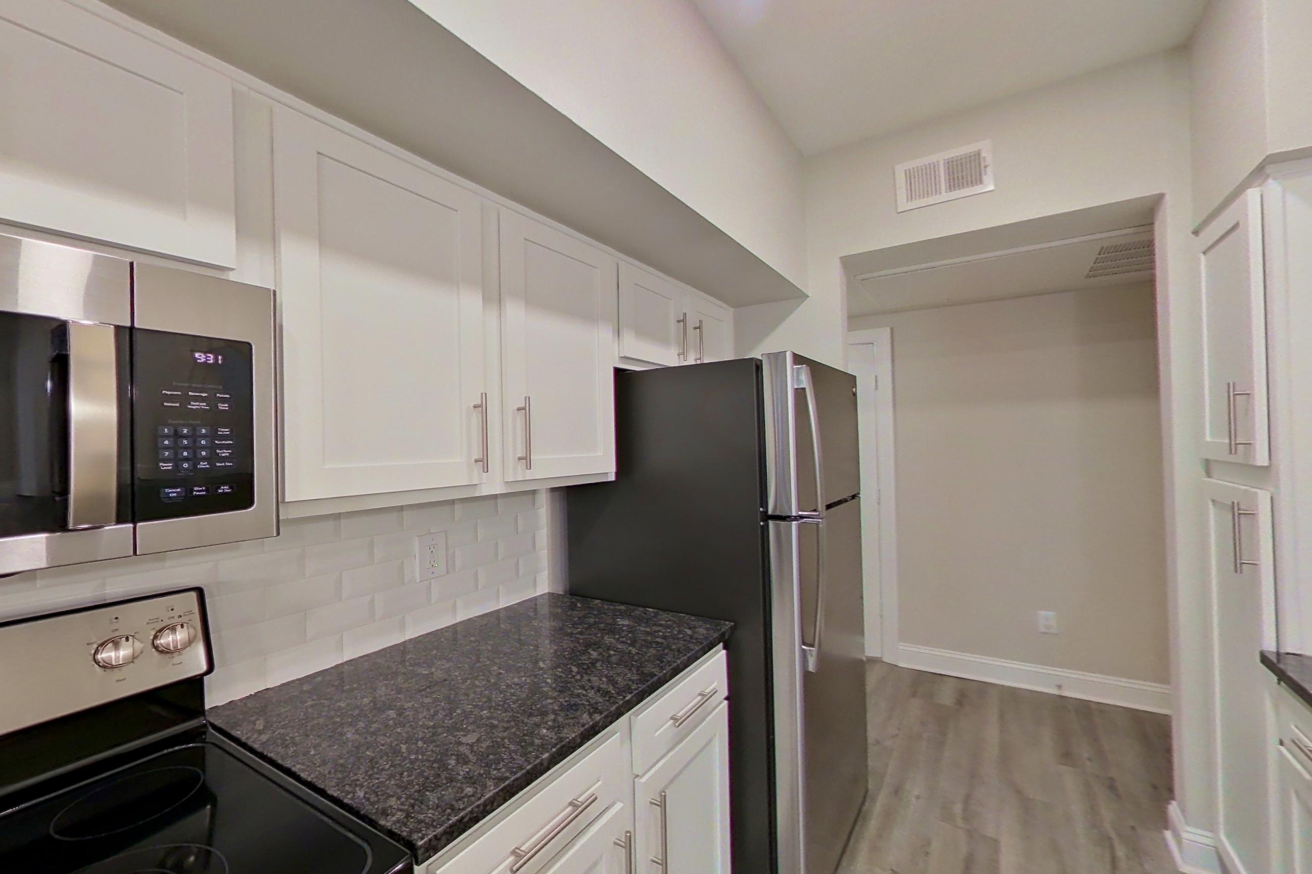 Kitchen with dark stone countertops, dishwasher, electric range, light countertops, light wood-finish flooring, microwave, oven/range, refrigerator, and stainless steel appliances, Apartment 2211 at Marq Perimeter