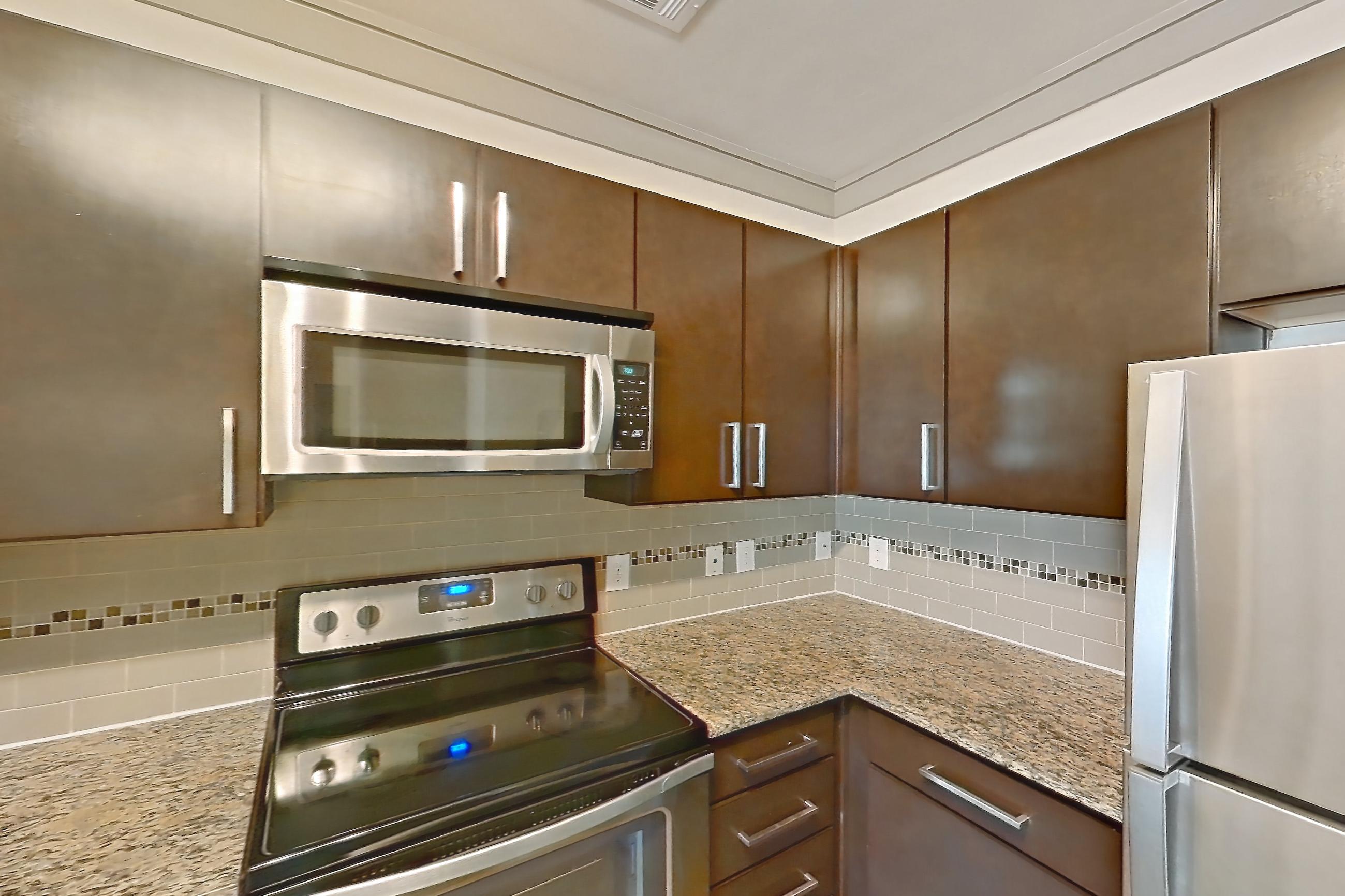 Kitchen with dishwasher, electric range, light carpet, light countertops, light stone countertops, light wood-finish flooring, microwave, oven/range, and stainless steel appliances, Apartment 3312 at Marquis Seven Meadows