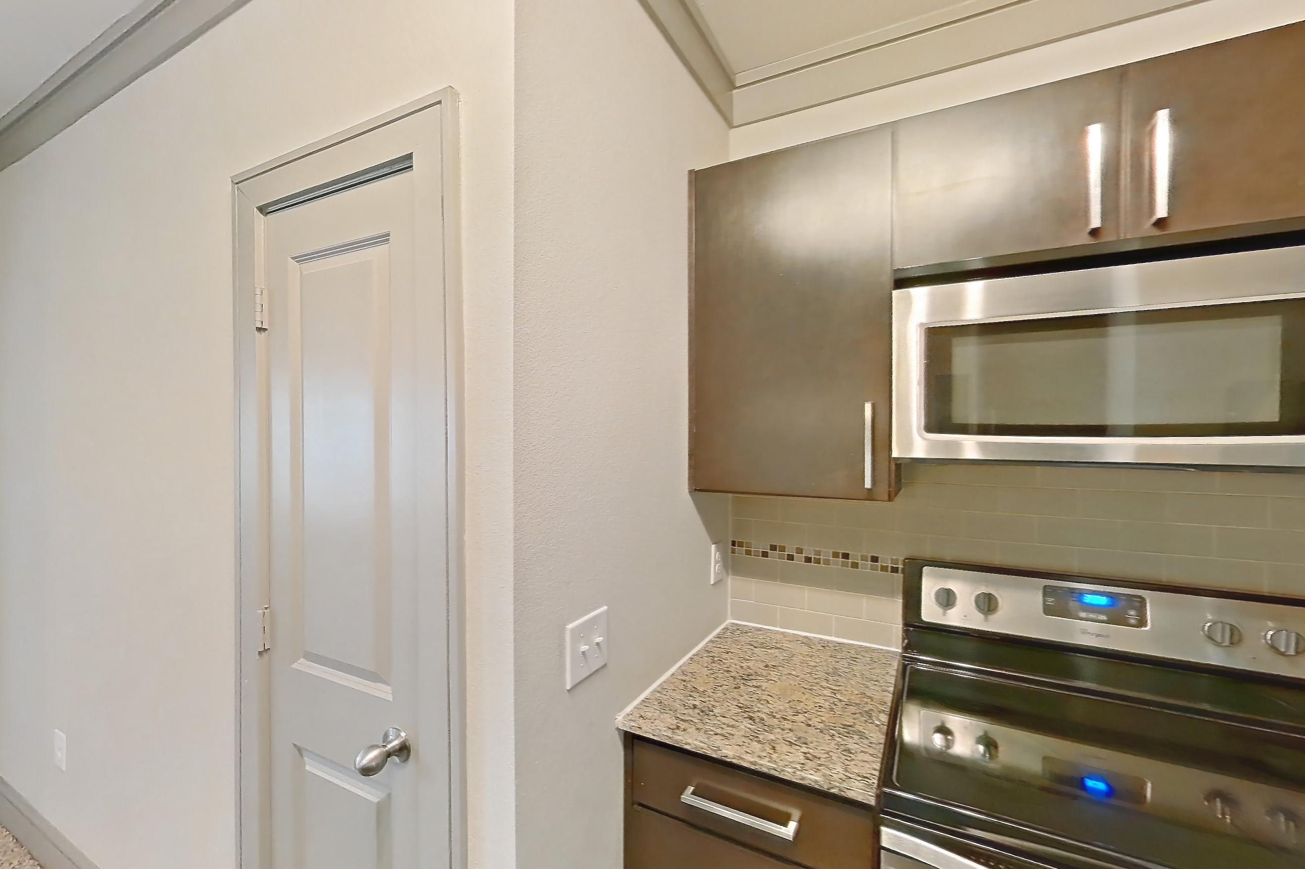 Kitchen with dishwasher, electric range, light carpet, light countertops, light stone countertops, light wood-finish flooring, microwave, oven/range, and stainless steel appliances, Apartment 3312 at Marquis Seven Meadows