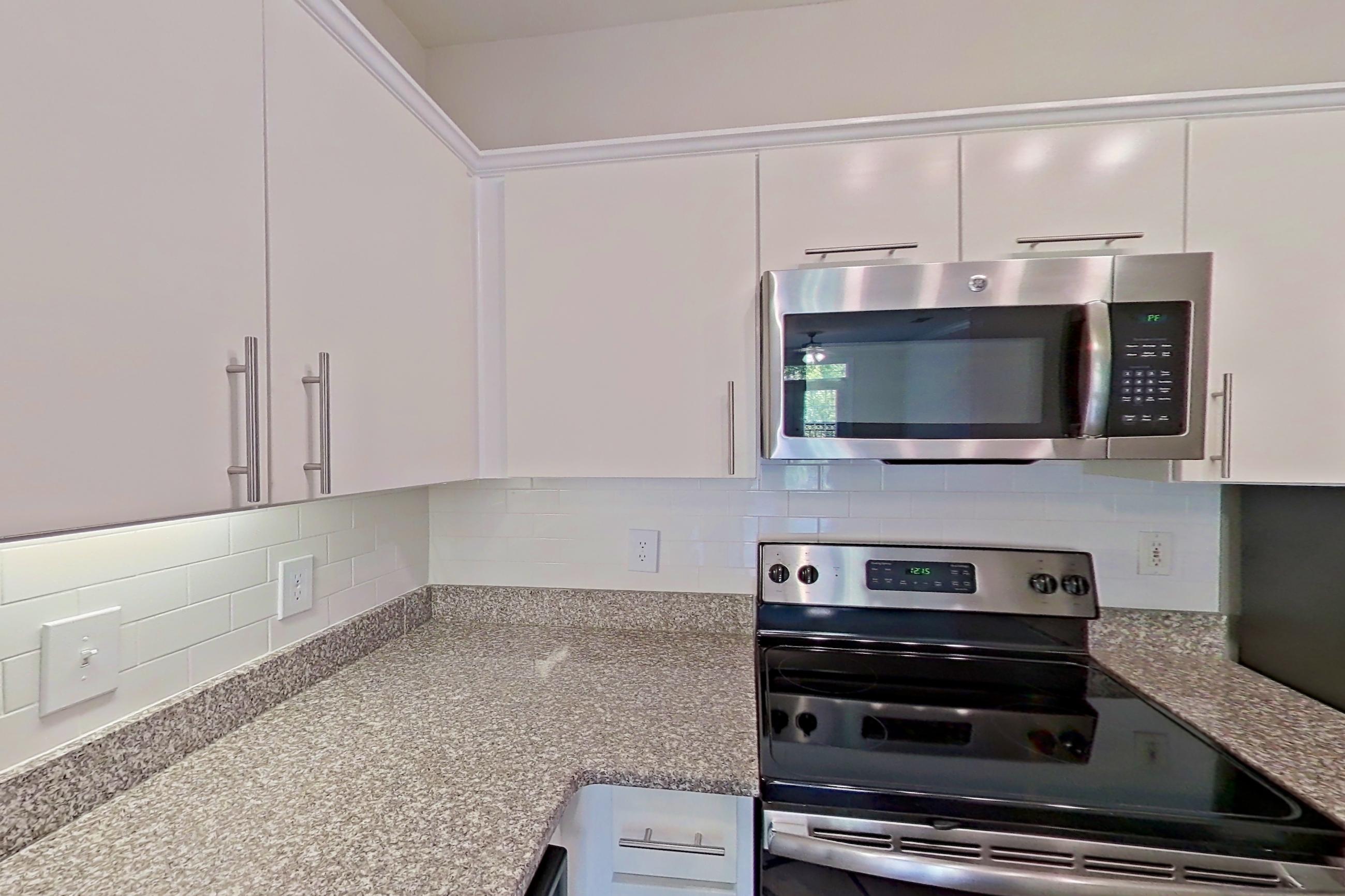 Kitchen with dark wood-finish flooring, electric range, light countertops, light stone countertops, microwave, oven/range, refrigerator, and stainless steel appliances, Apartment 2514 at Marq Perimeter