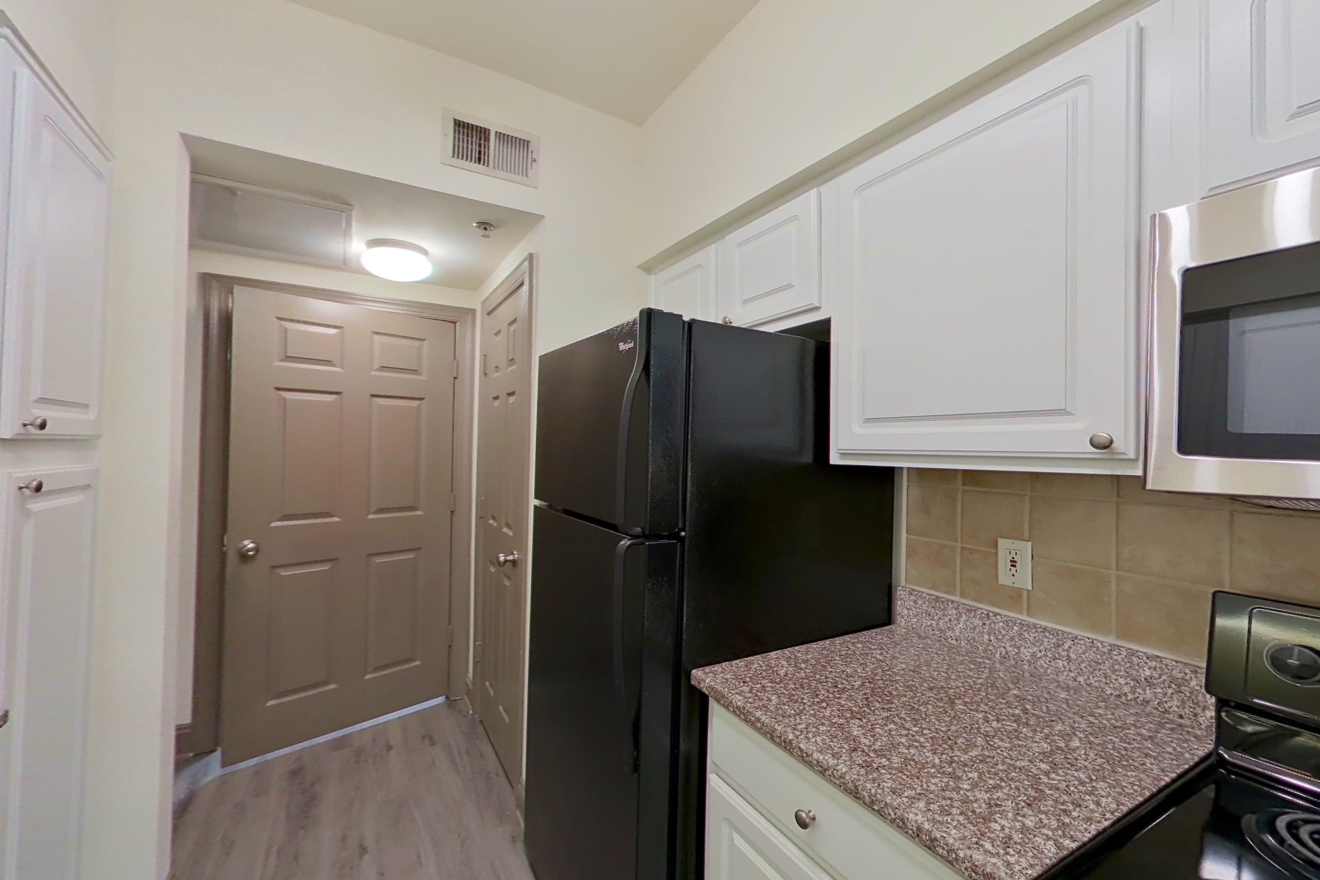 Kitchen with black appliances, dishwasher, electric range, light countertops, light stone countertops, light wood-finish flooring, microwave, oven/range, refrigerator, and stainless steel appliances, Apartment 3110 at Marq Perimeter