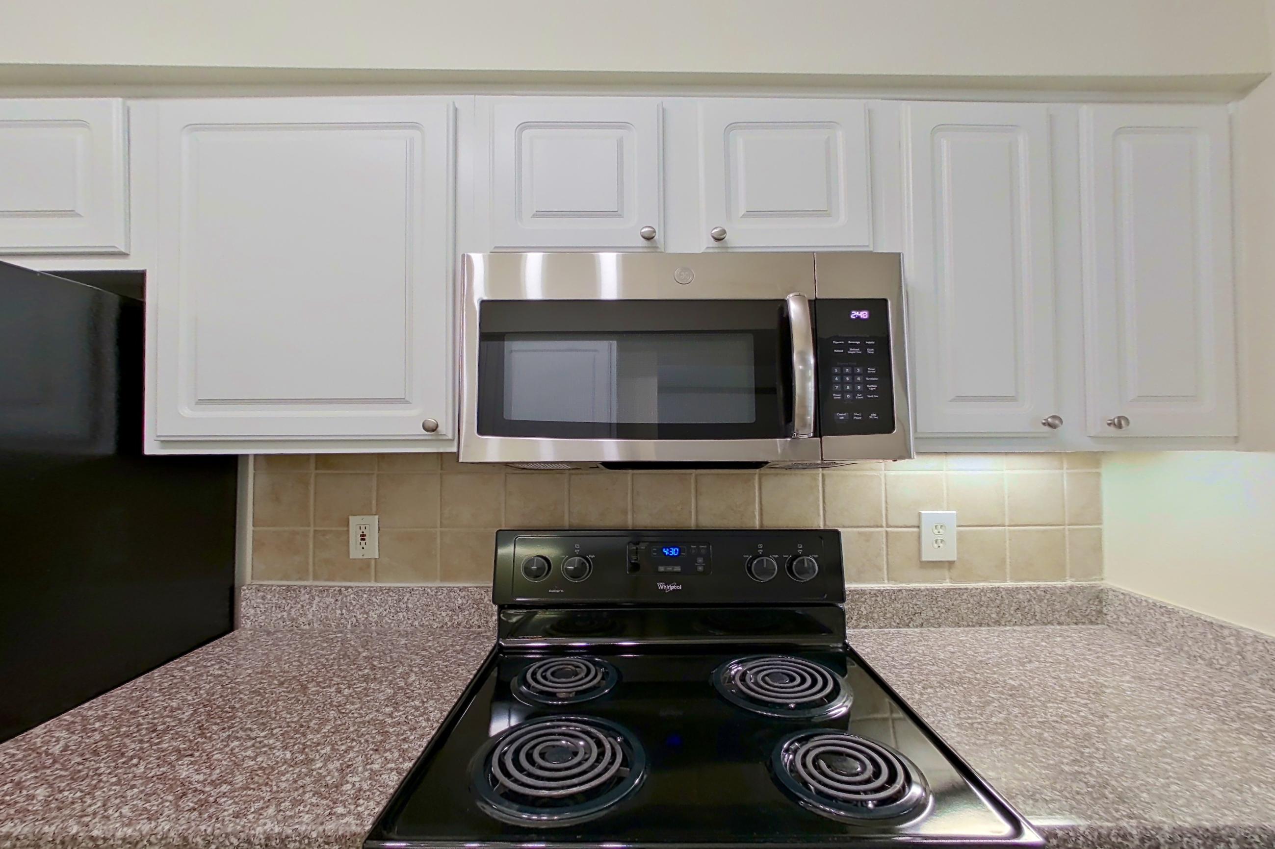 Kitchen with black appliances, dishwasher, electric range, light countertops, light stone countertops, light wood-finish flooring, microwave, oven/range, refrigerator, and stainless steel appliances, Apartment 3110 at Marq Perimeter