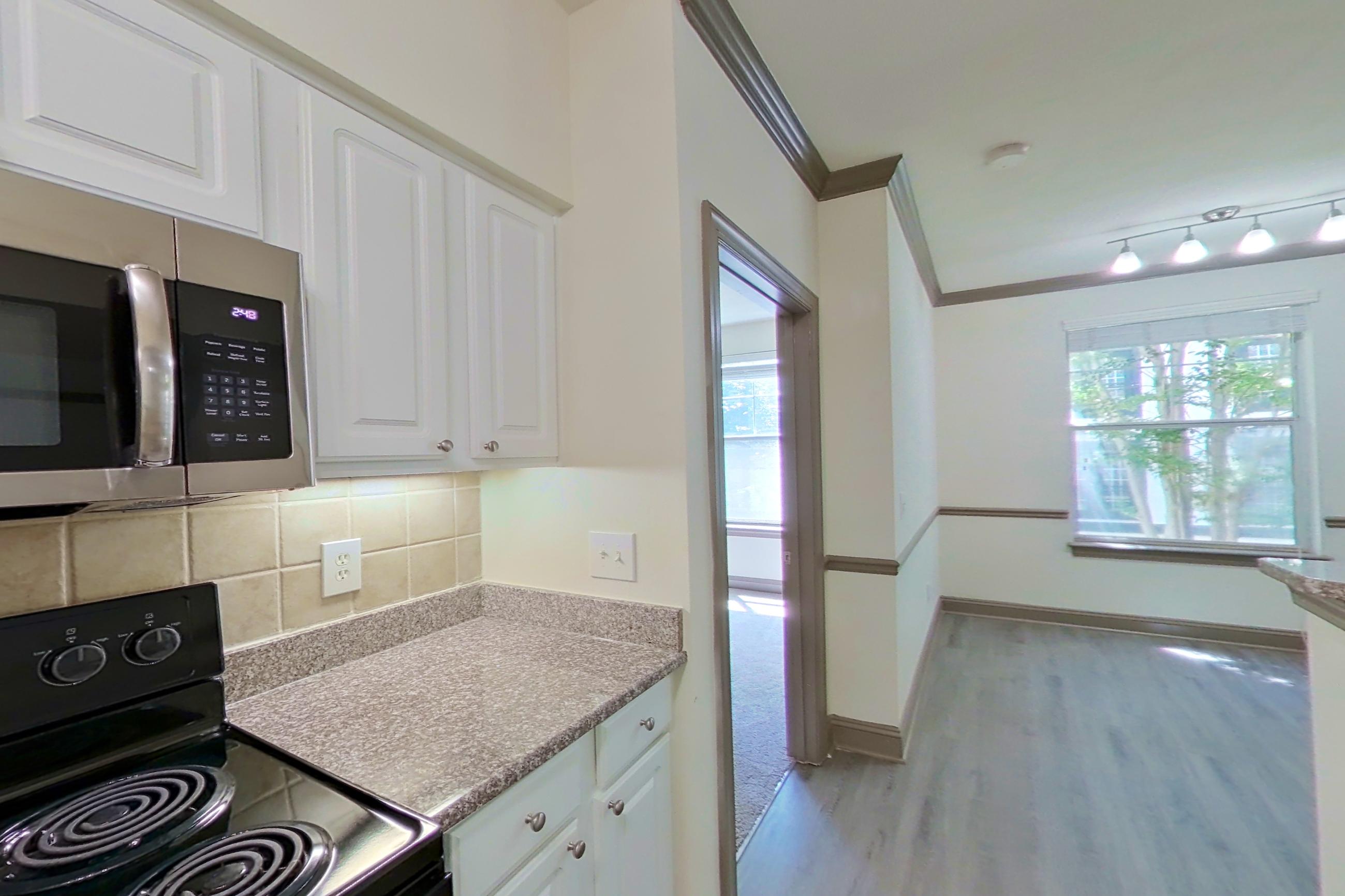 Kitchen with black appliances, dishwasher, electric range, light countertops, light stone countertops, light wood-finish flooring, microwave, oven/range, refrigerator, and stainless steel appliances, Apartment 3110 at Marq Perimeter