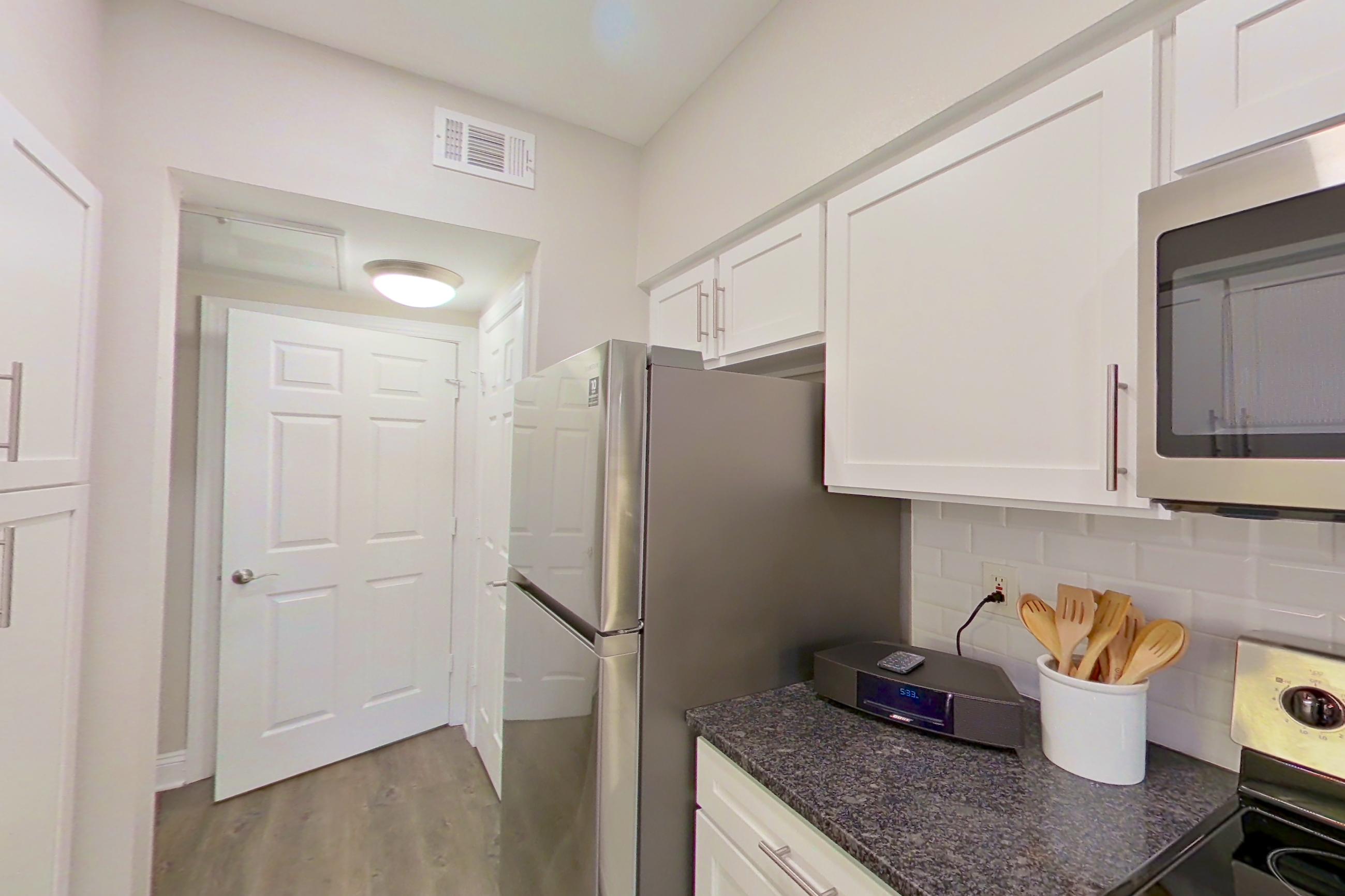 Kitchen with dark stone countertops, dishwasher, electric range, light countertops, light wood-finish flooring, oven/range, refrigerator, and stainless steel appliances, Apartment 3201 at Marq Perimeter