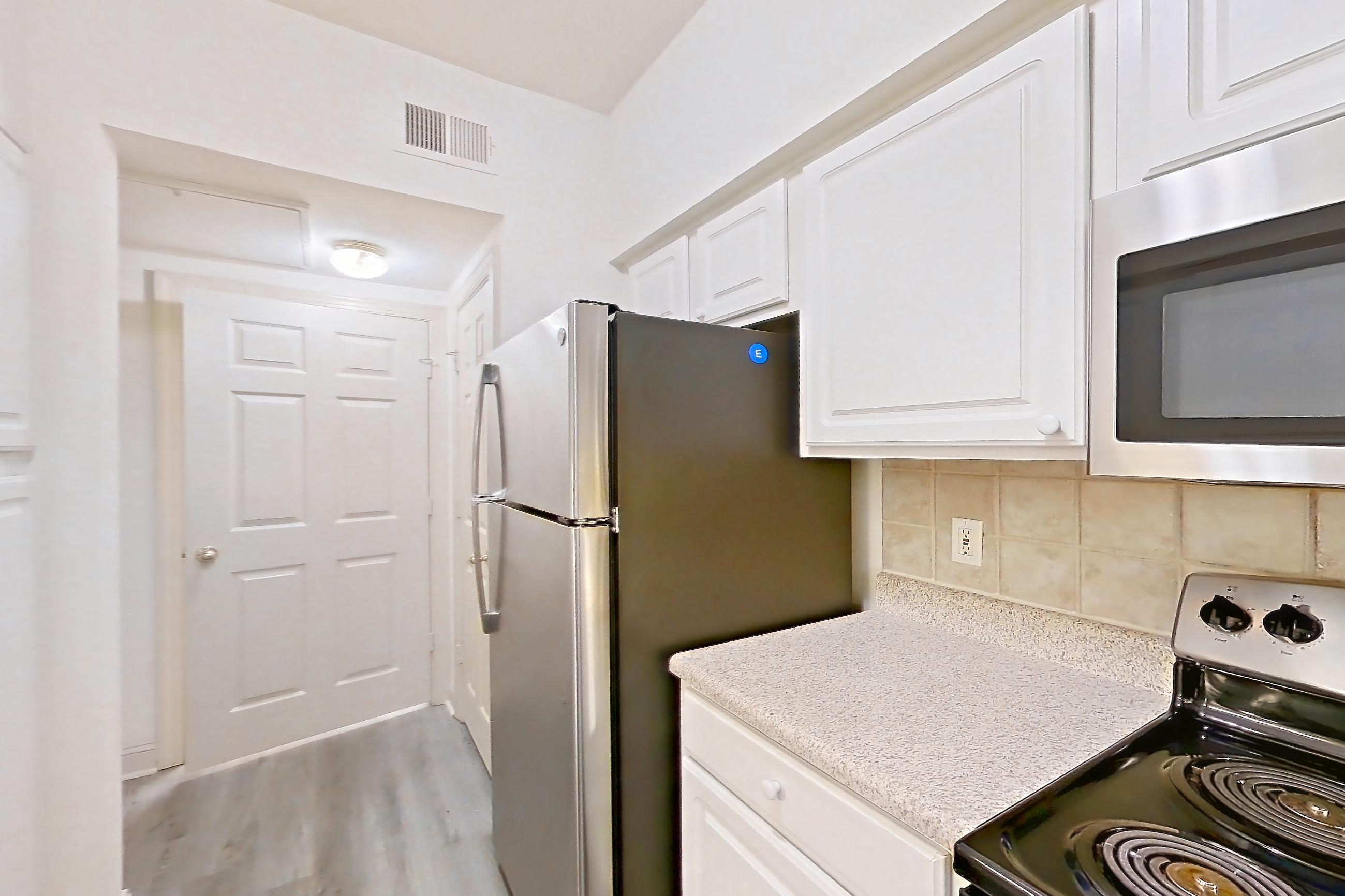 Kitchen with dishwasher, electric range, light countertops, light stone countertops, light wood-finish flooring, microwave, oven/range, refrigerator, and stainless steel appliances, Apartment 3205 at Marq Perimeter