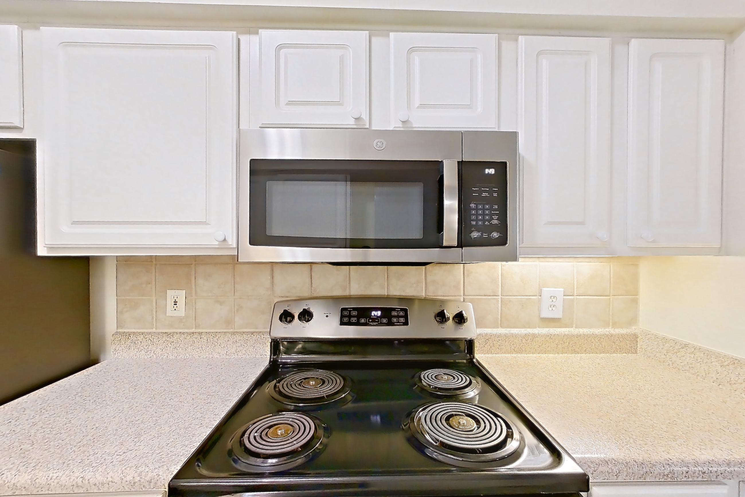 Kitchen with dishwasher, electric range, light countertops, light stone countertops, light wood-finish flooring, microwave, oven/range, refrigerator, and stainless steel appliances, Apartment 3205 at Marq Perimeter