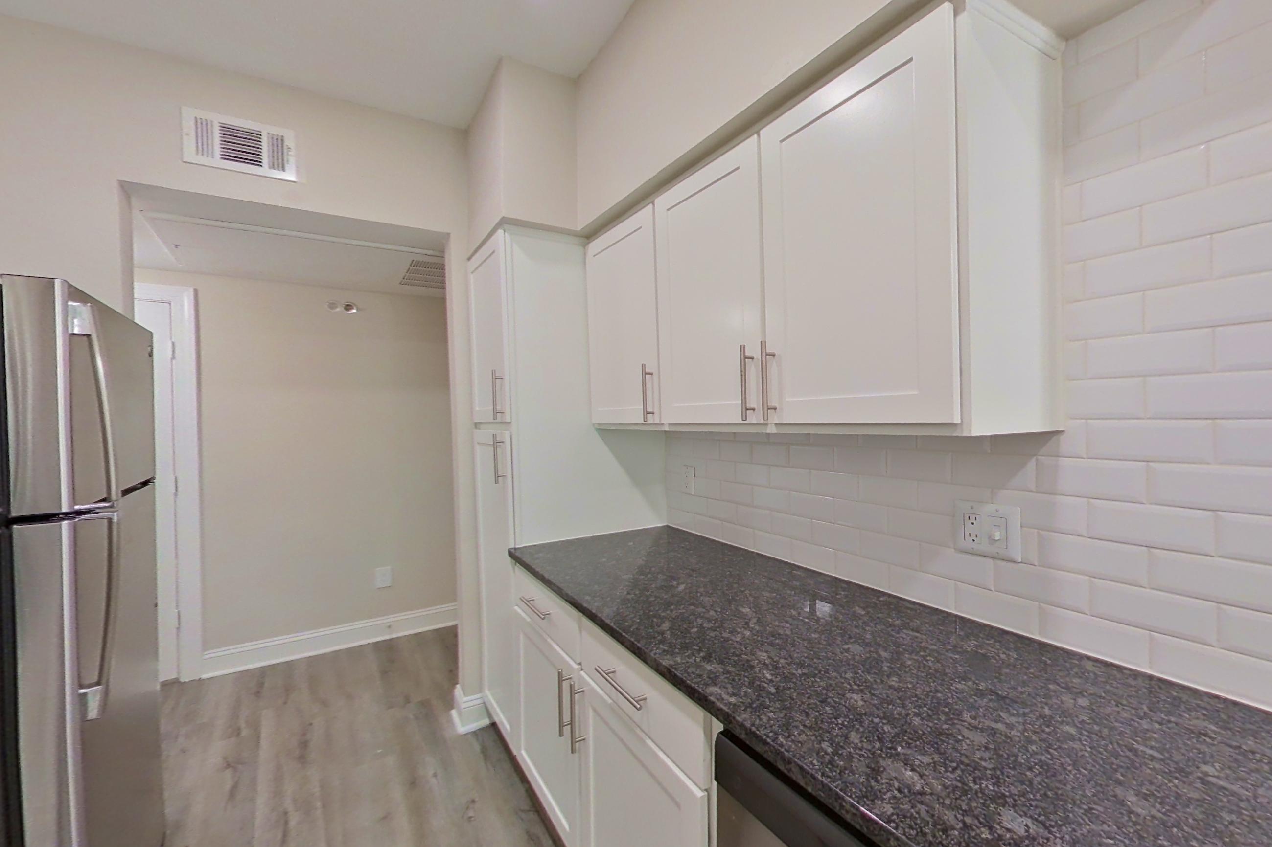 Kitchen with dark stone countertops, dishwasher, electric range, light countertops, light wood-finish flooring, oven/range, refrigerator, and stainless steel appliances, Apartment 3206 at Marq Perimeter