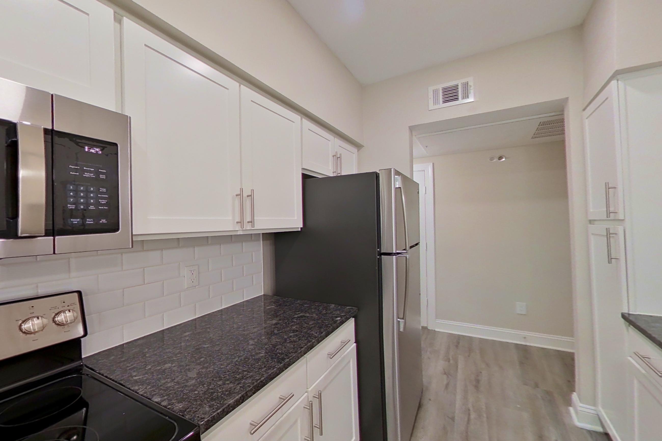 Kitchen with dark stone countertops, dishwasher, electric range, light countertops, light wood-finish flooring, oven/range, refrigerator, and stainless steel appliances, Apartment 3206 at Marq Perimeter