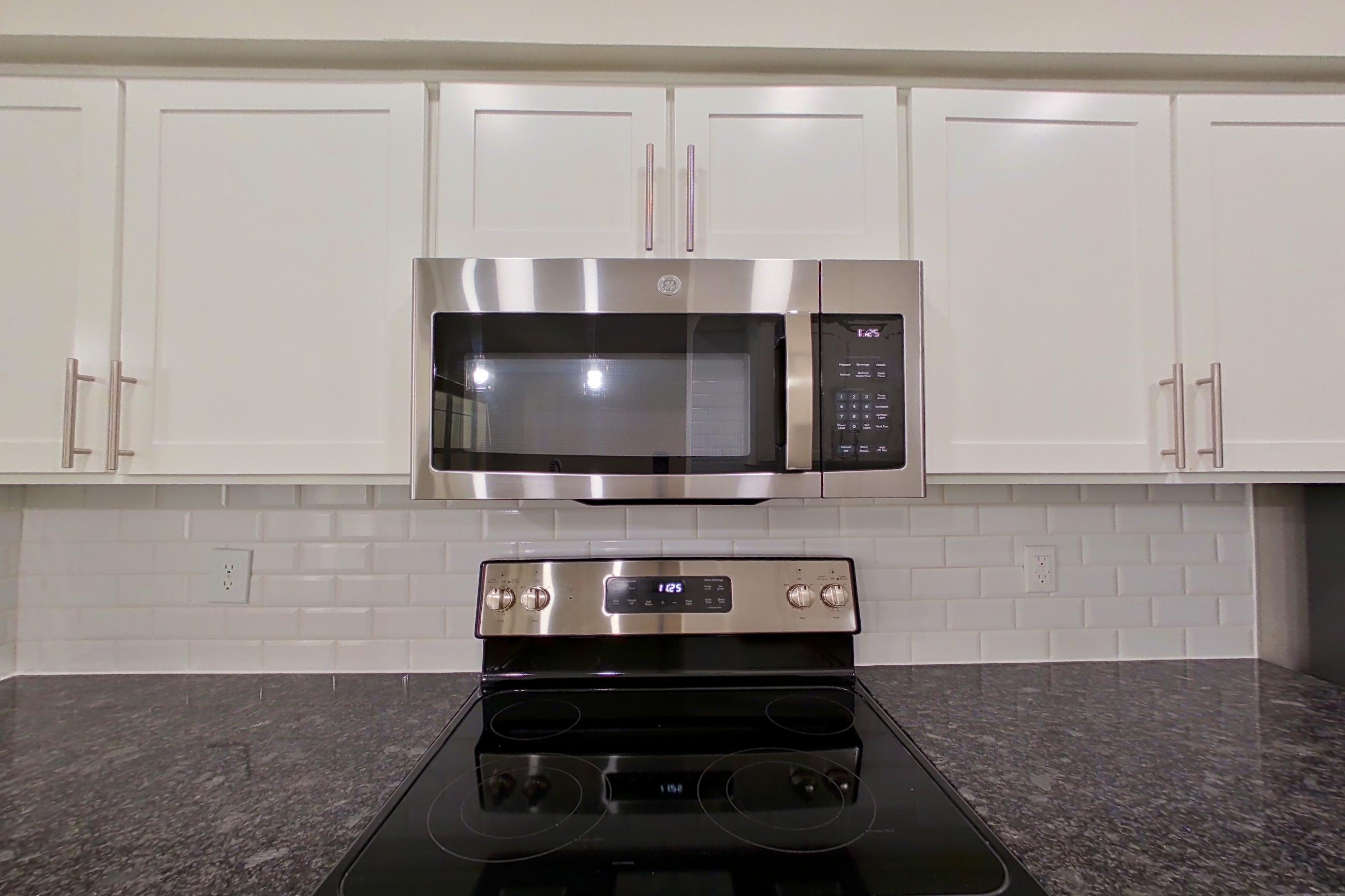 Kitchen with dark stone countertops, dishwasher, electric range, light countertops, light wood-finish flooring, oven/range, refrigerator, and stainless steel appliances, Apartment 3206 at Marq Perimeter