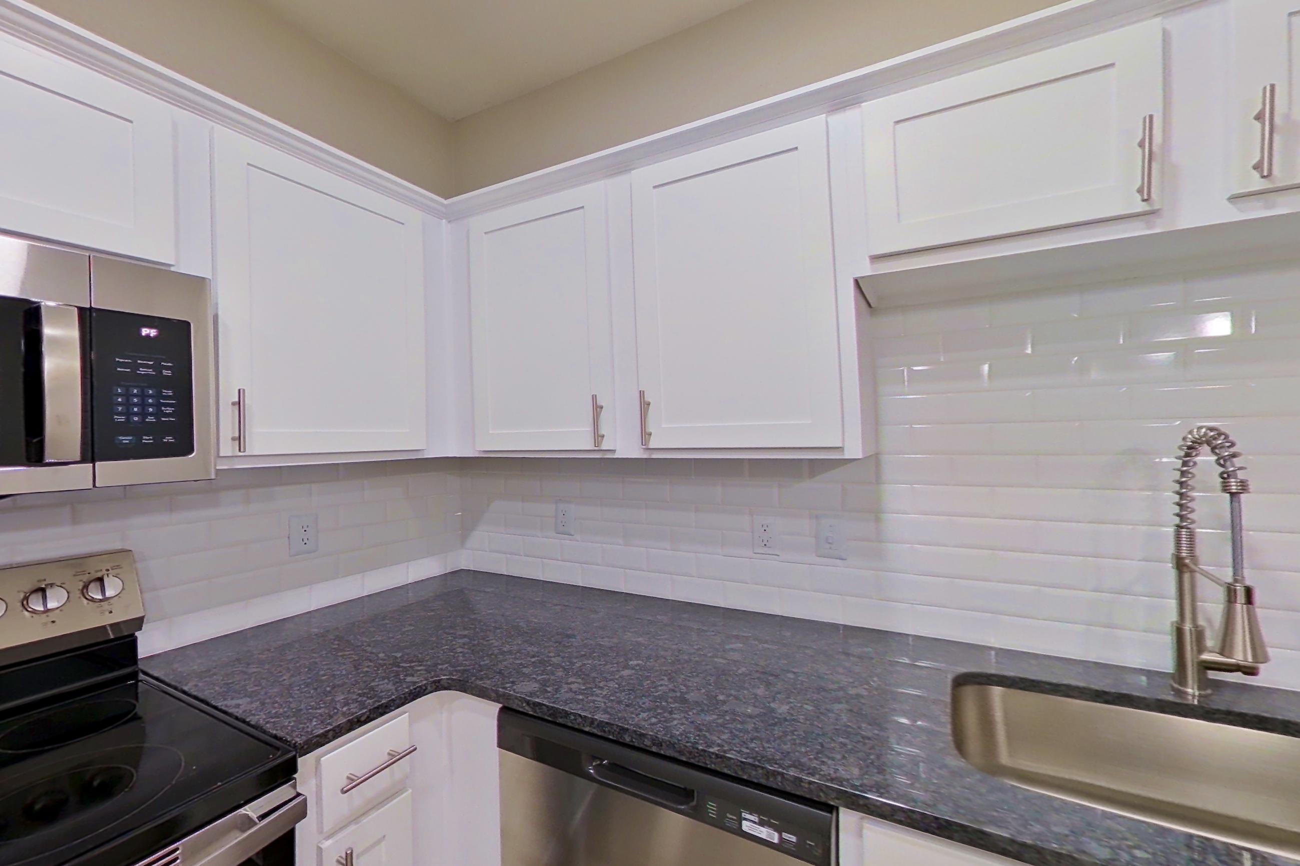 Kitchen with dark stone countertops, dishwasher, electric range, light wood-finish flooring, microwave, oven/range, refrigerator, and stainless steel appliances, Apartment 3213 at Marq Perimeter