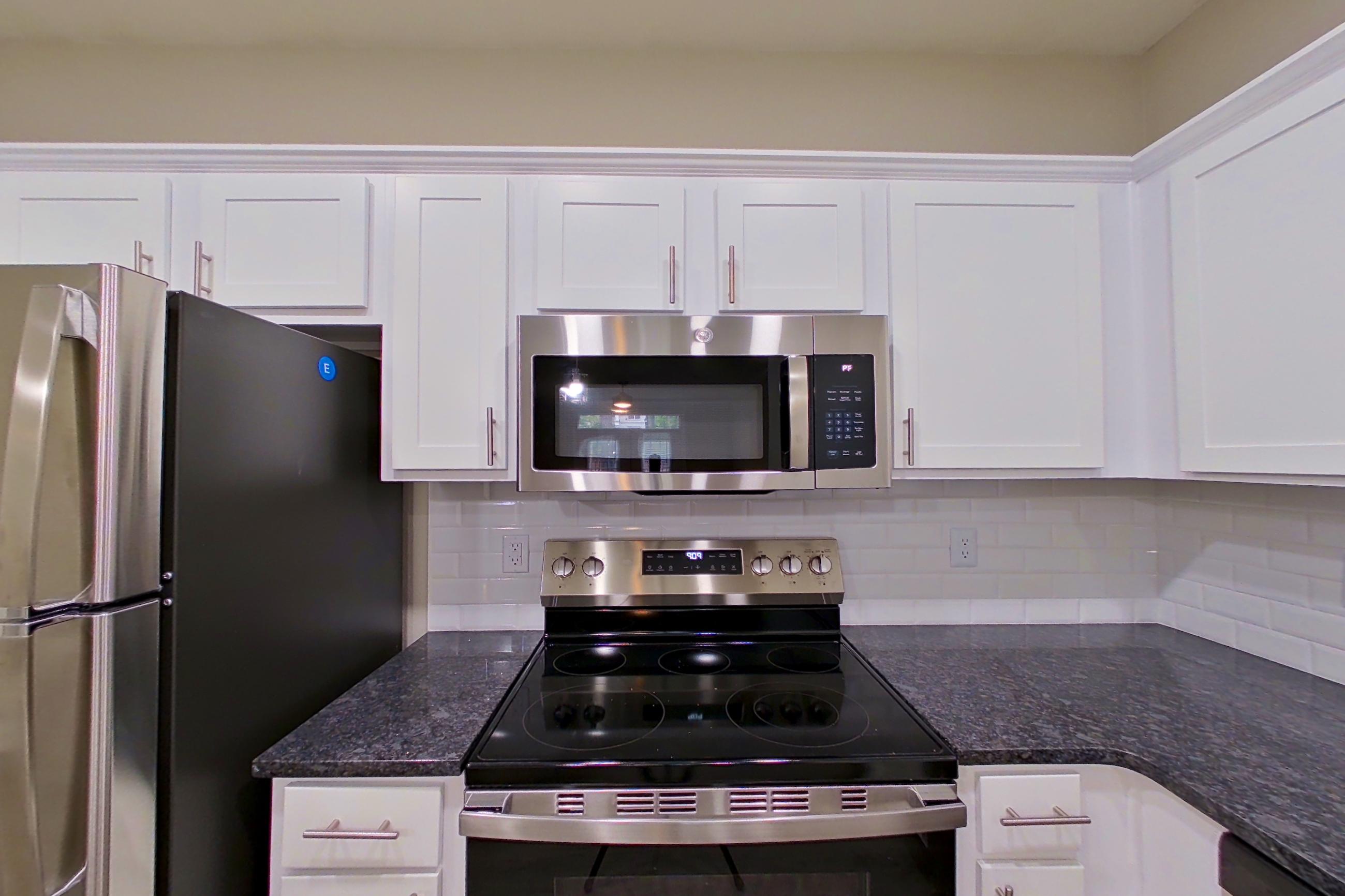 Kitchen with dark stone countertops, dishwasher, electric range, light wood-finish flooring, microwave, oven/range, refrigerator, and stainless steel appliances, Apartment 3213 at Marq Perimeter